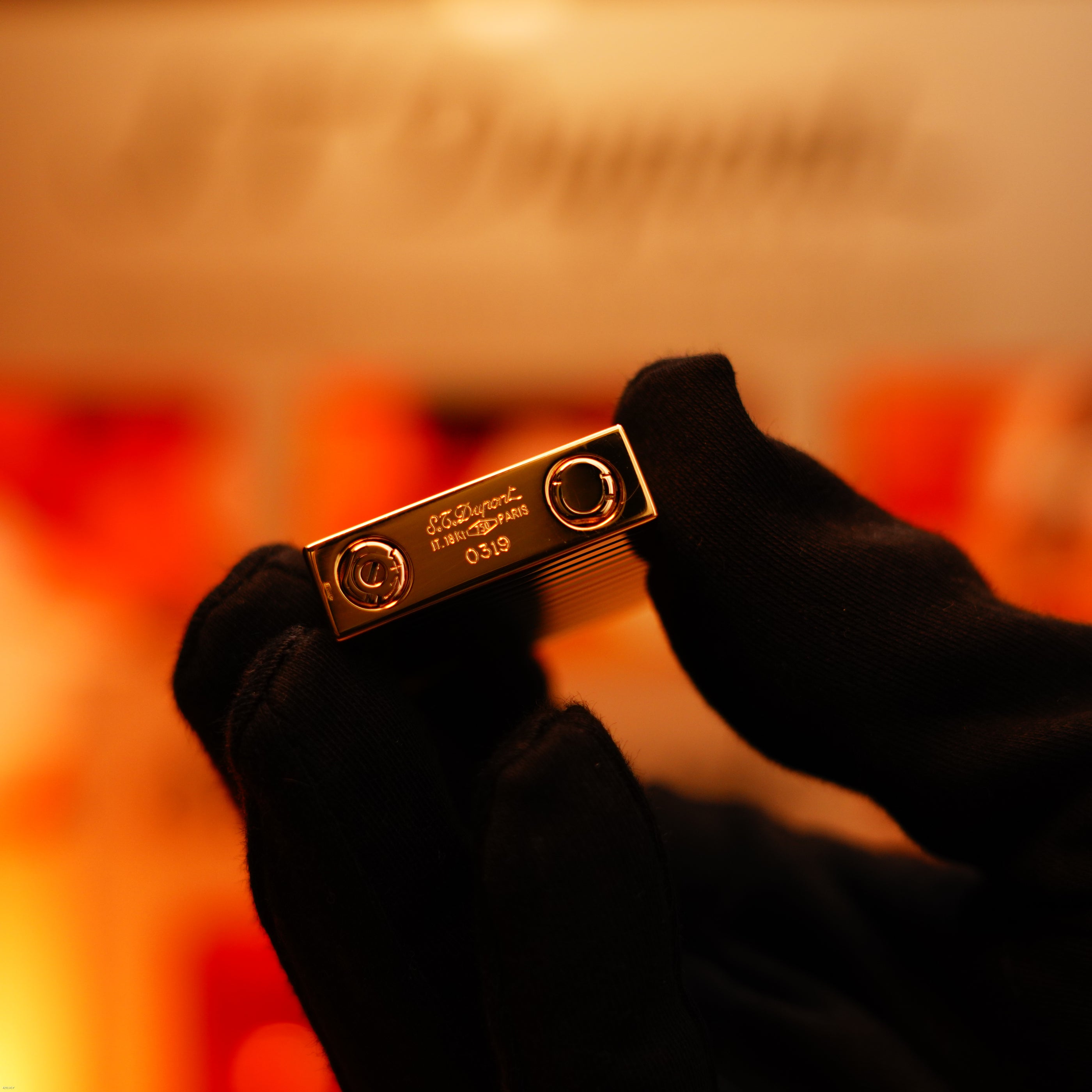 A gloved hand holds the Vintage 1970 Ultra Rare 1/1 ST Dupont Lighter by Lucy Lighter, crafted from solid 18K gold, against a warm, blurred background—an exquisite display of timeless elegance and craftsmanship.