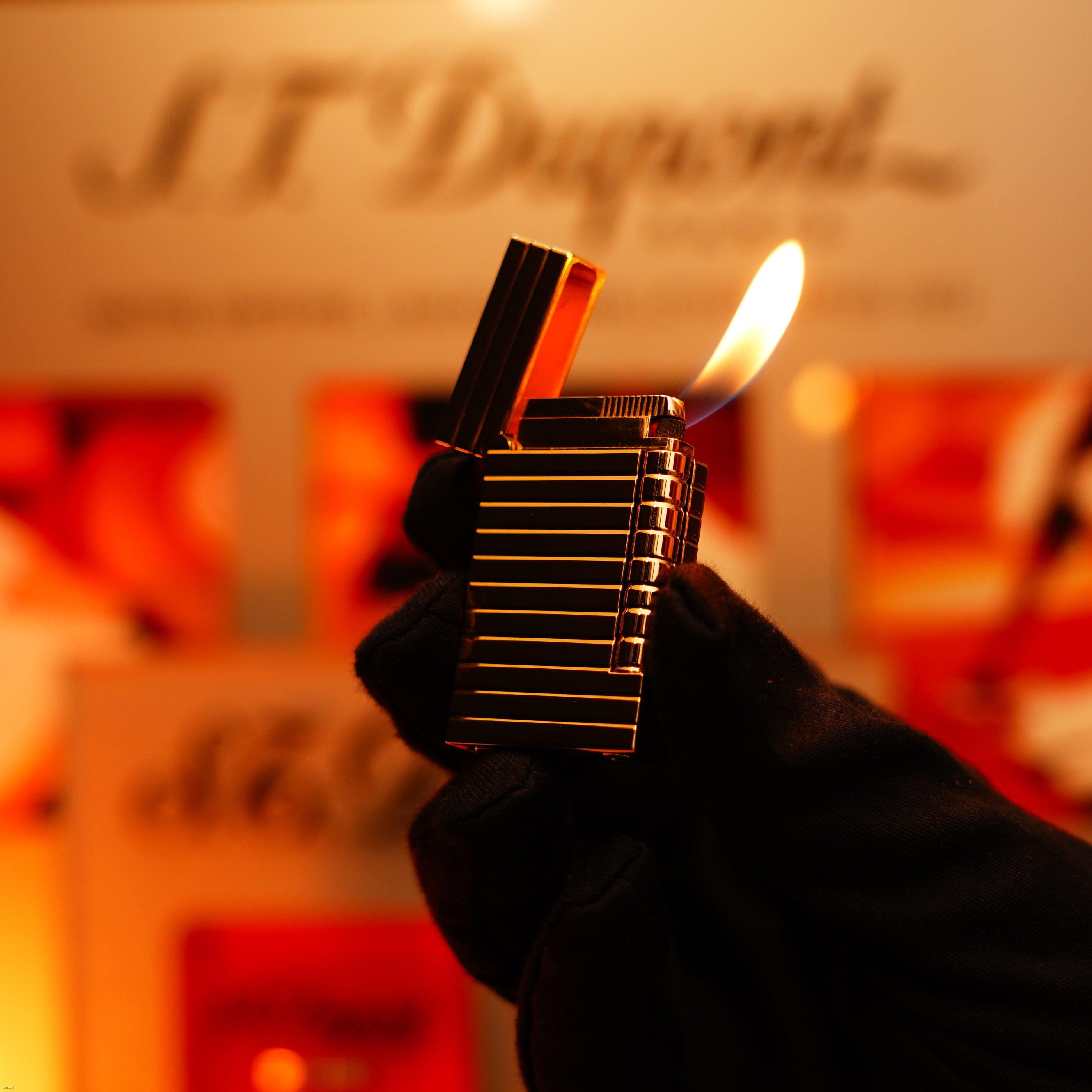 A gloved hand holds the Vintage 1970 Ultra Rare 1/1 ST Dupont Lighter – Solid 18K Gold Masterpiece by Lucy Lighter, its lid open and flame lit, with a blurred S.T. Dupont sign in the background.
