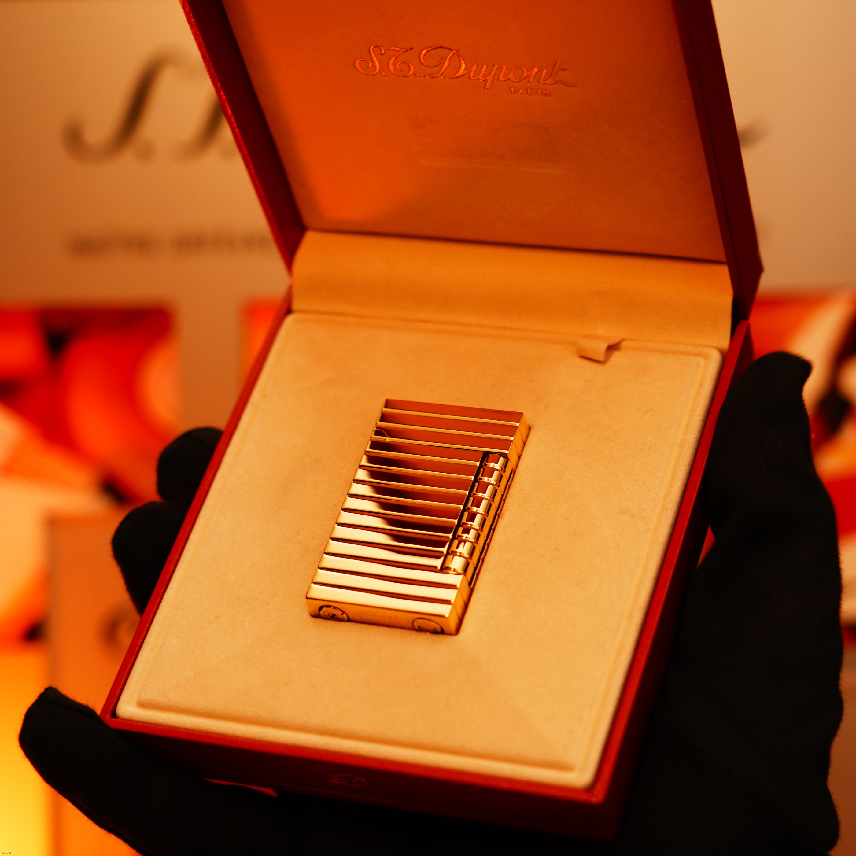 A gloved hand holds an open box with the Vintage 1970 Ultra Rare 1/1 ST Dupont Lighter – Solid 18K Gold Masterpiece by Lucy Lighter, elegantly displayed on a beige cushion to showcase its rarity and luxury.