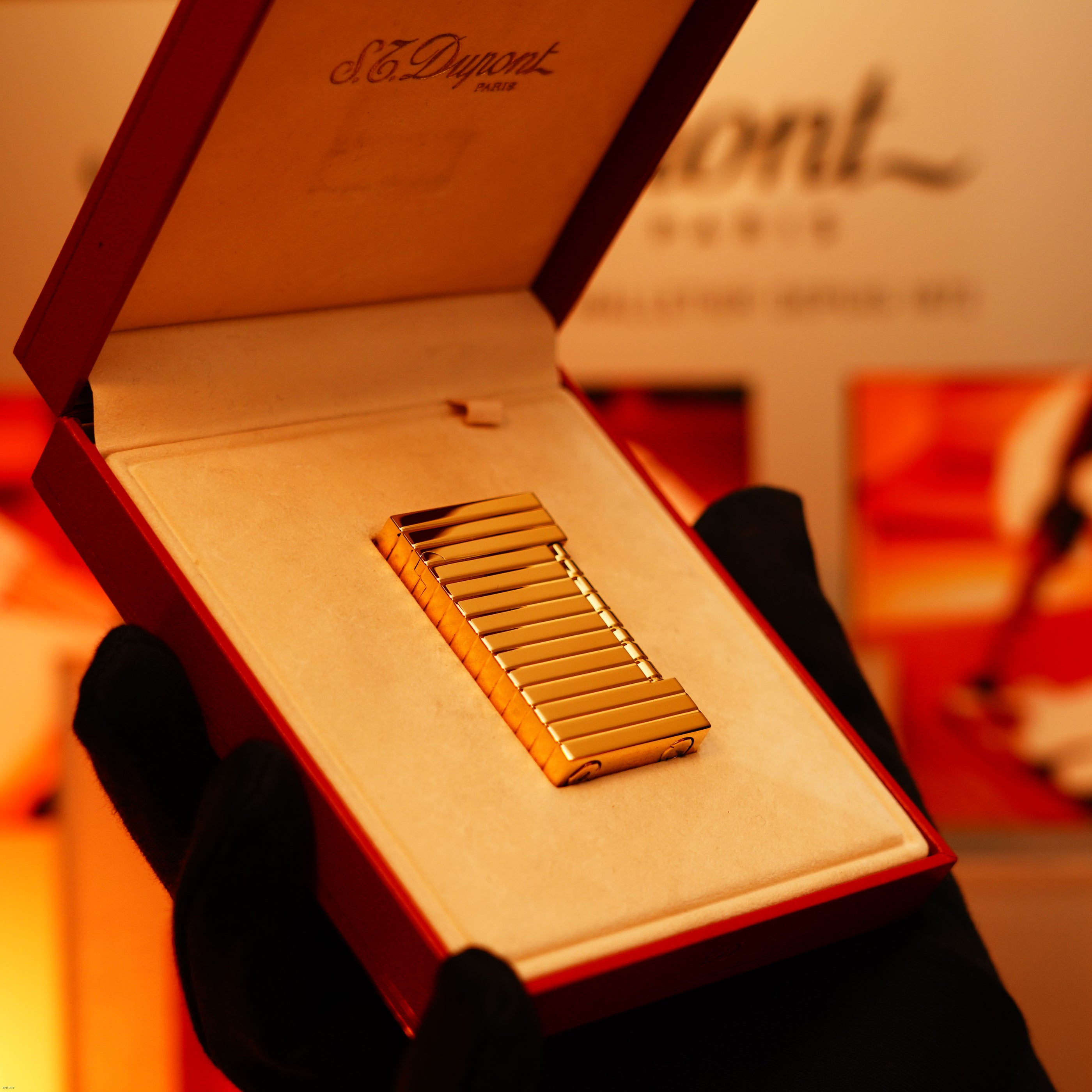 A gloved hand holds an open red box revealing the Vintage 1970 Ultra Rare ST Dupont Lighter—Solid 18K Gold Masterpiece by Lucy Lighter, a showcase of timeless luxury and exquisite craftsmanship.