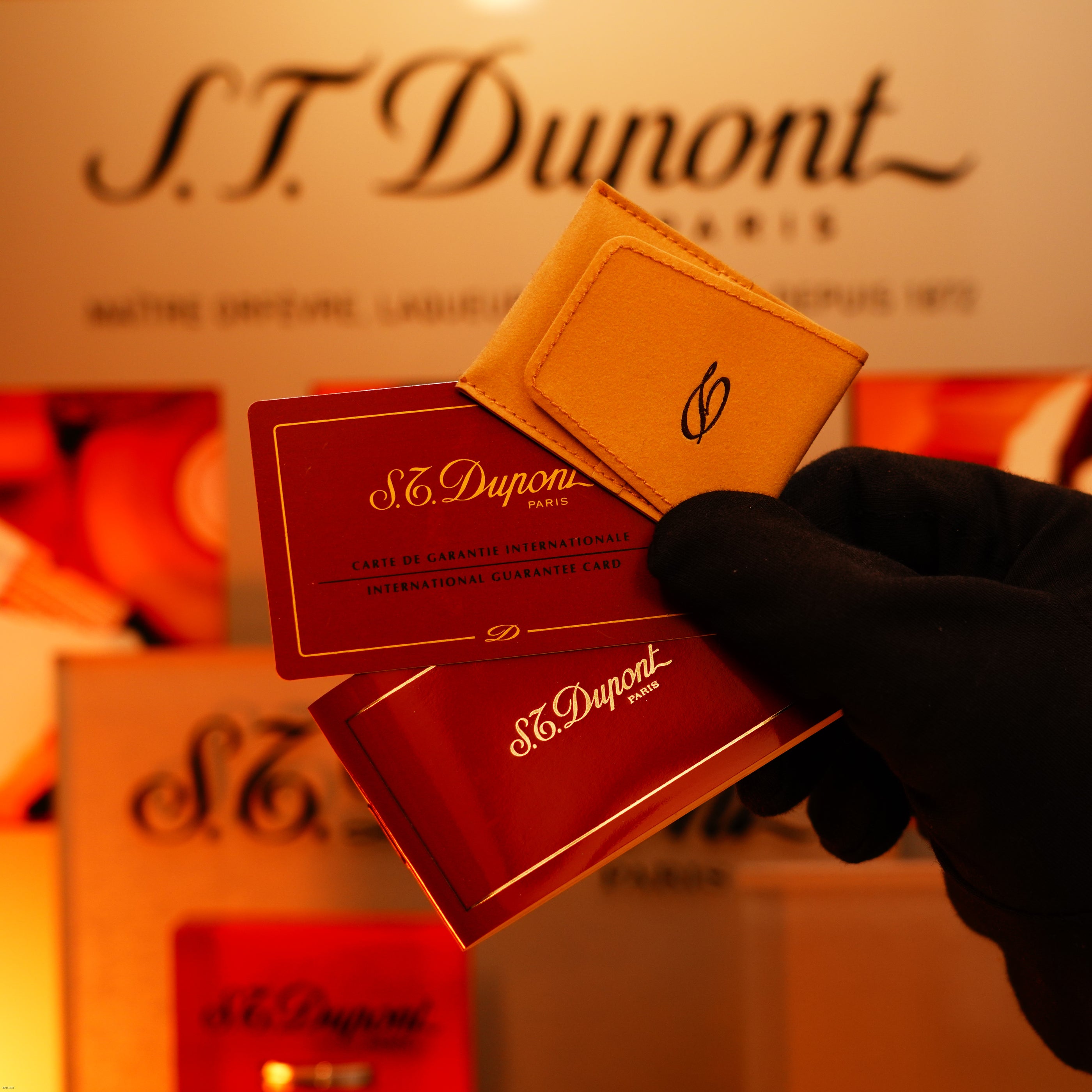 A gloved hand holds Lucy Lighter guarantee cards and a tan card holder, with branded packaging in the background—highlighting the exclusive Vintage 1970 Ultra Rare 1/1 ST Dupont Lighter made from solid 18K gold.
