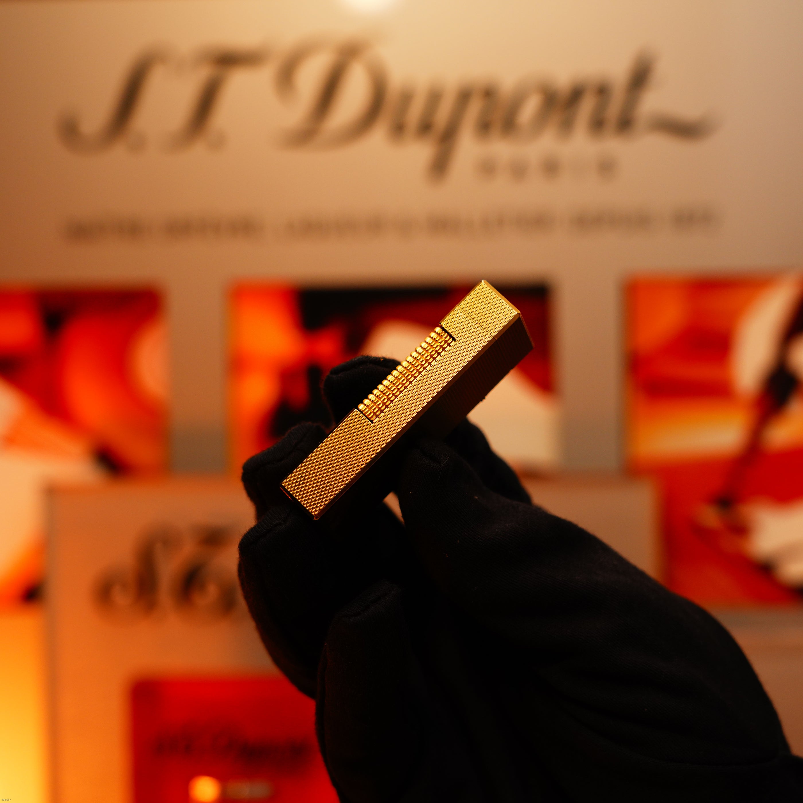 A gloved hand holds a vintage 1975 Dunhill 24k heavy gold finish barley pattern lighter by Lucy Lighter against a blurred background, highlighting its timeless elegance and guaranteed quality.