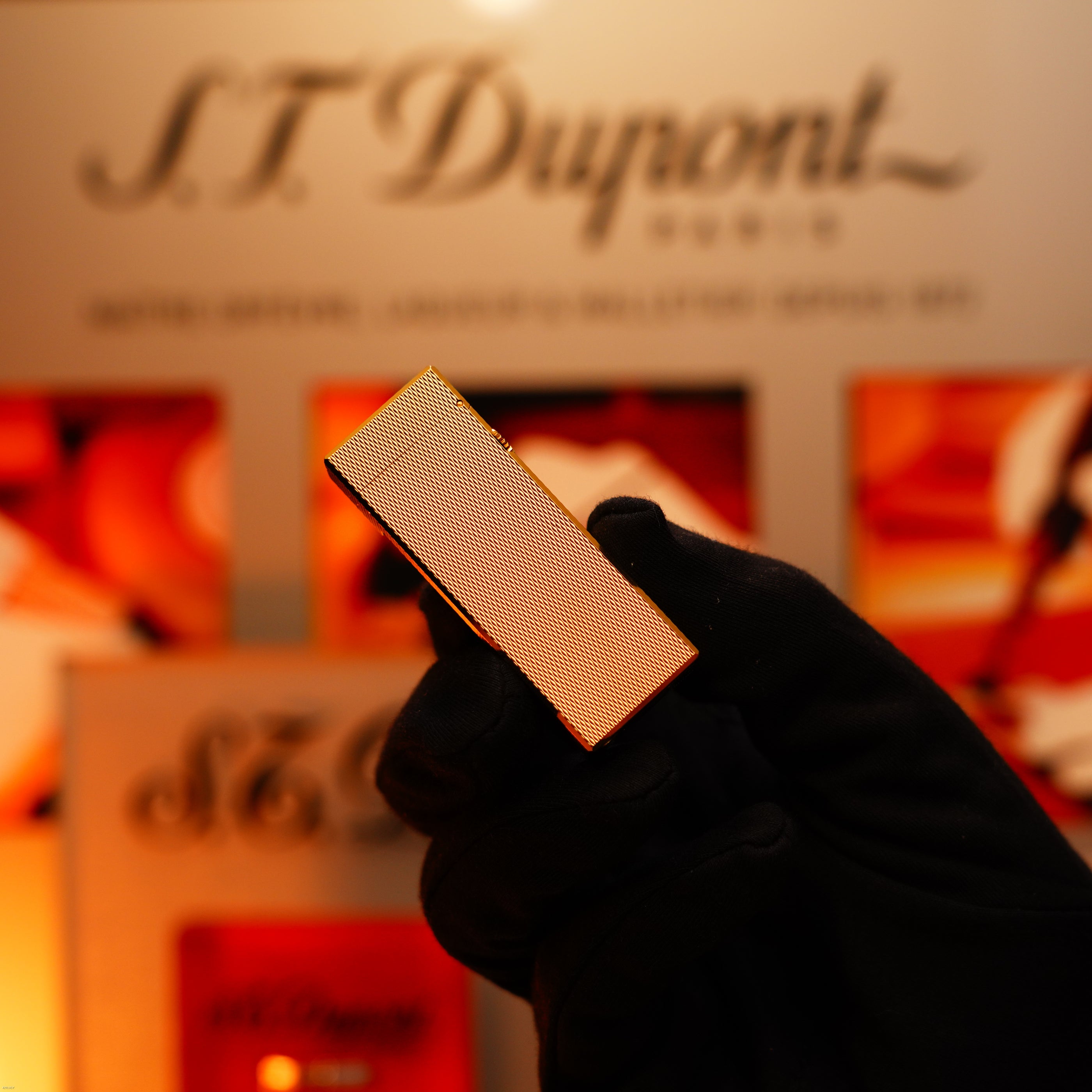 A gloved hand holds a Vintage 1975 Dunhill 24k Heavy Gold Finish Barley Pattern Early Version Lighter by Lucy Lighter, with logo and packaging visible, highlighting its quality guarantee and 12-month warranty.