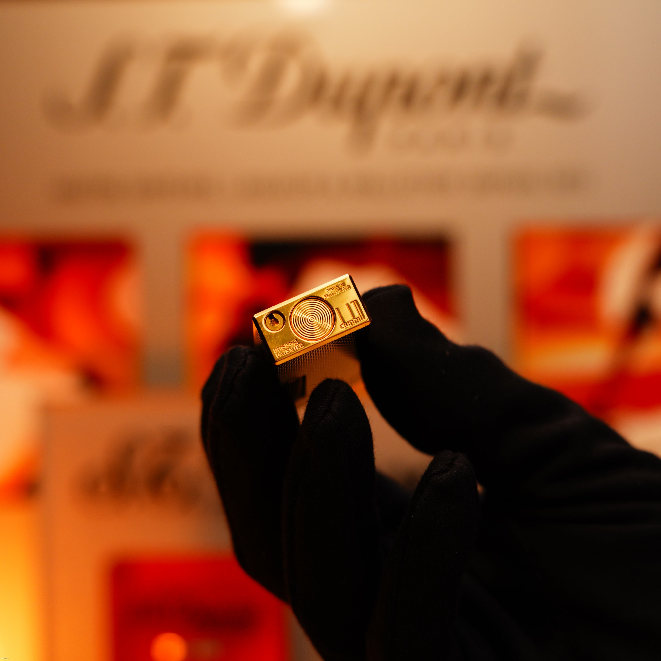 A gloved hand holds a Vintage 1975 Dunhill 24k Heavy Gold Finish Barley Pattern Early Version Lighter by Lucy Lighter against a blurred background, showcasing its timeless elegance and exquisite craftsmanship.
