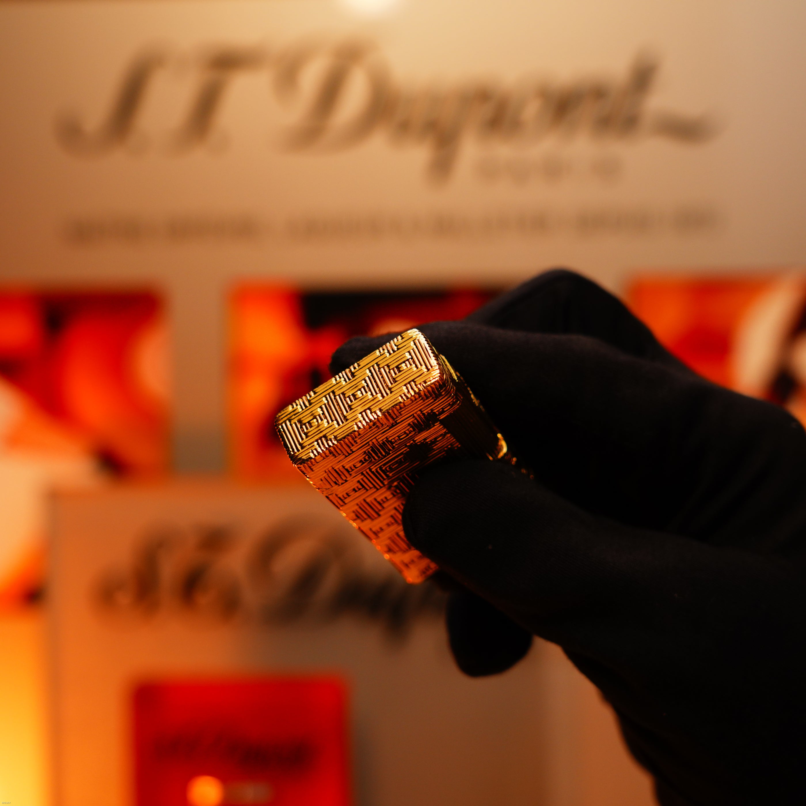 A gloved hand holds a Lucy Lighter Vintage 1960 Extremely Rare 1/1 St Dupont Lighter—solid 18K gold, heavy early edition, 750 hallmarked—in front of an S.T. Dupont display.