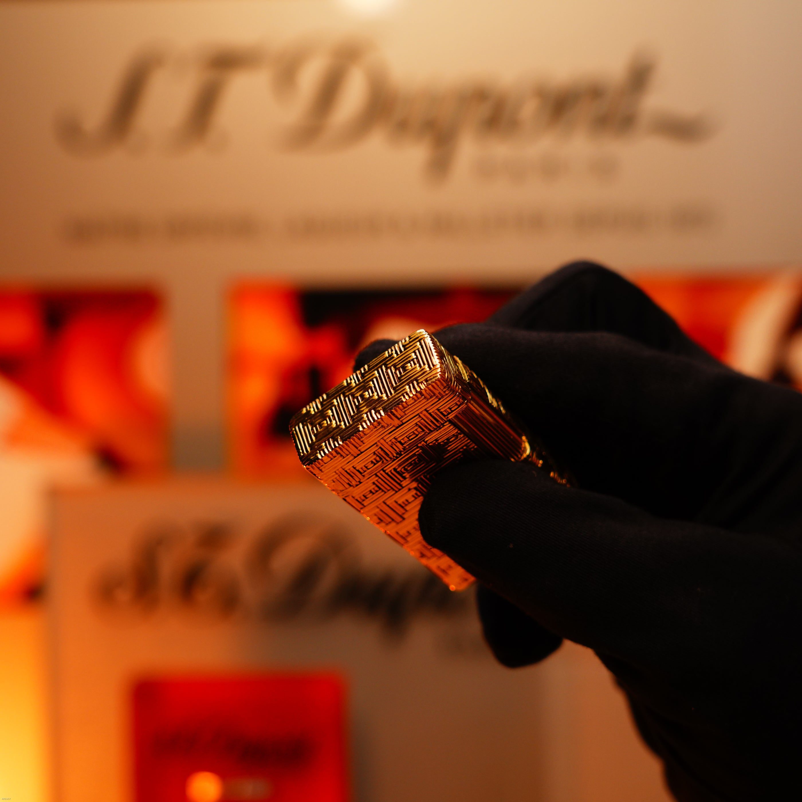 A gloved hand holds a Lucy Lighter Vintage 1960 Extremely Rare 1/1 St Dupont Lighter—Solid 18K Gold, Heavy Early Edition, 750 hallmarked—in front of a blurred display.