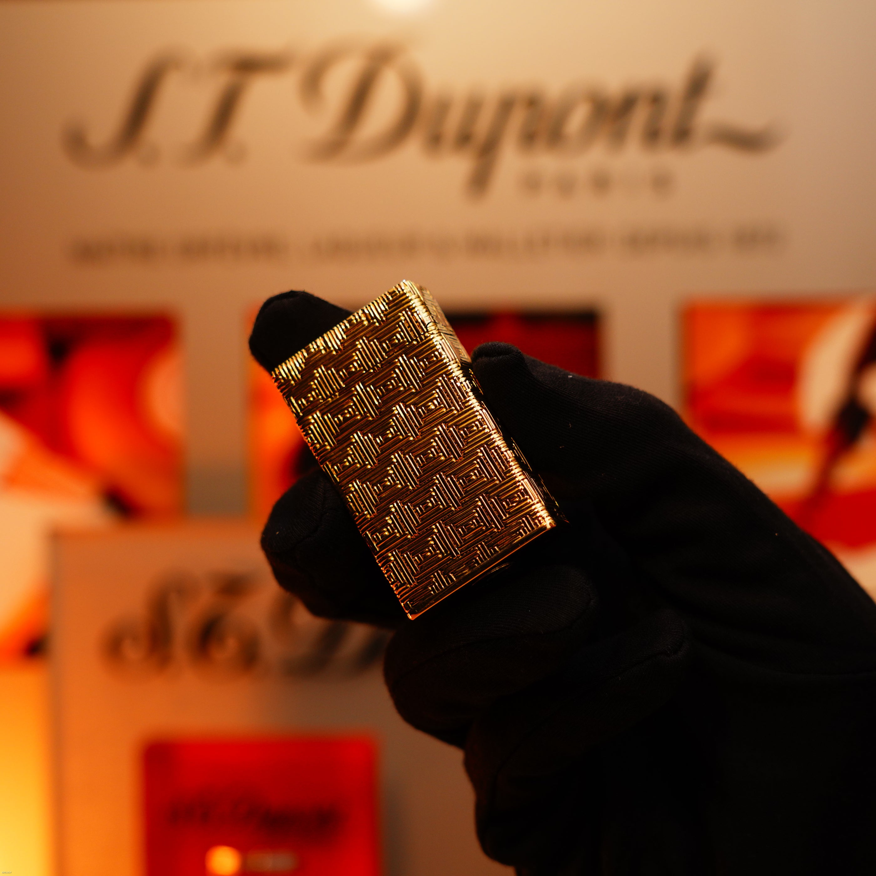 A gloved hand holds a Lucy Lighter Vintage 1960 Extremely Rare 1/1 St Dupont Lighter—solid 18K gold, heavy early edition, 750 hallmarked—in front of a blurred display background.