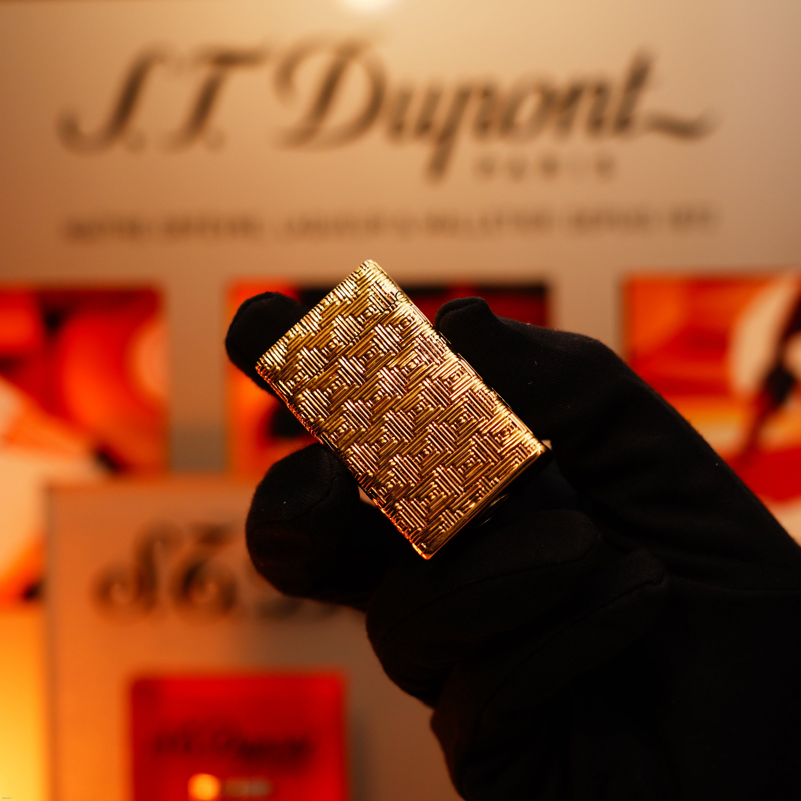 A gloved hand holds the Vintage 1960 Extremely Rare 1/1 St Dupont Lighter by Lucy Lighter—solid 18K gold, heavy early edition, 750 hallmarked—against a blurred S.T. Dupont logo and packaging in the background.