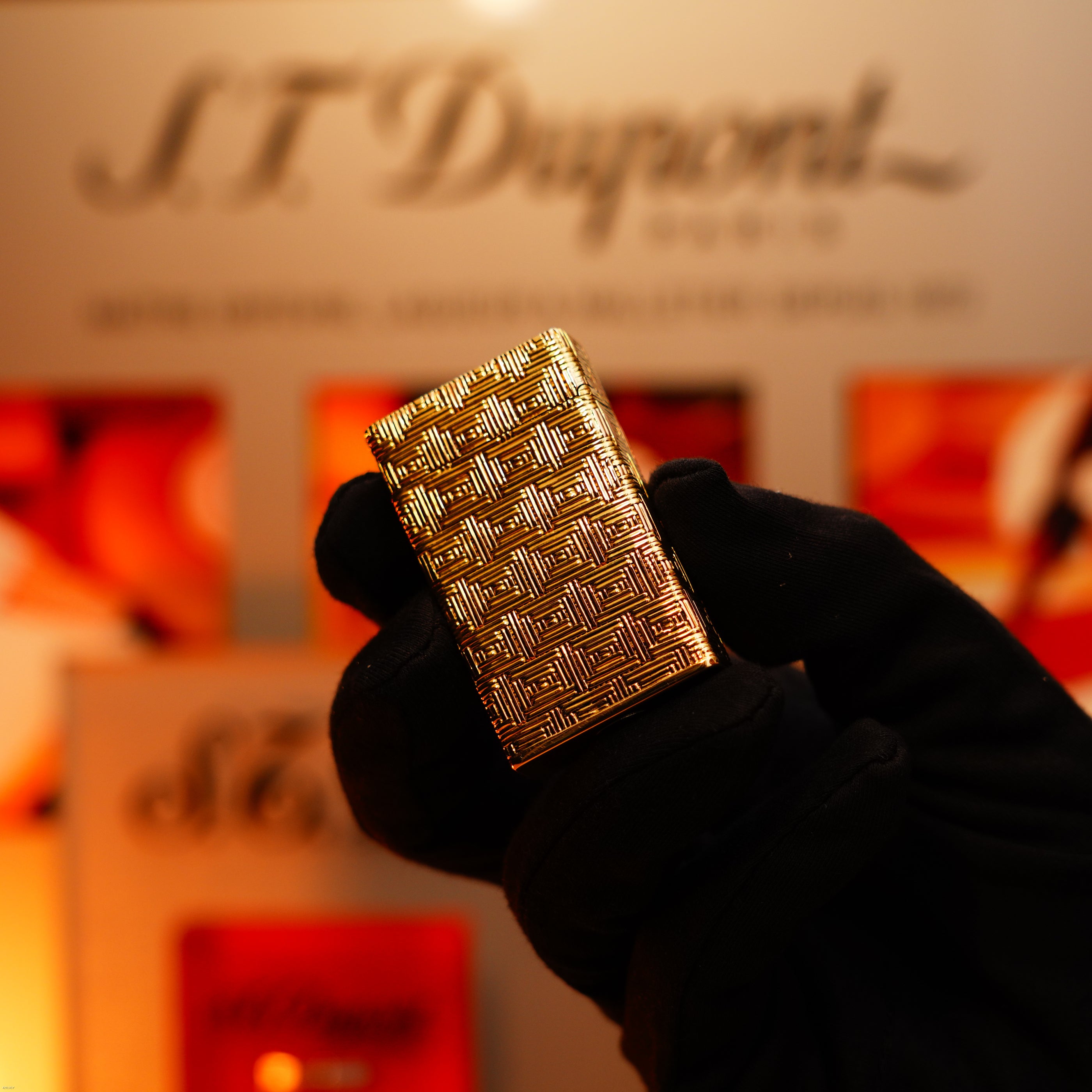 A gloved hand holds a solid 18K gold Vintage 1960 Extremely Rare 1/1 St Dupont Lighter by Lucy Lighter, heavy early edition with 750 hallmark, in front of a blurred display background.
