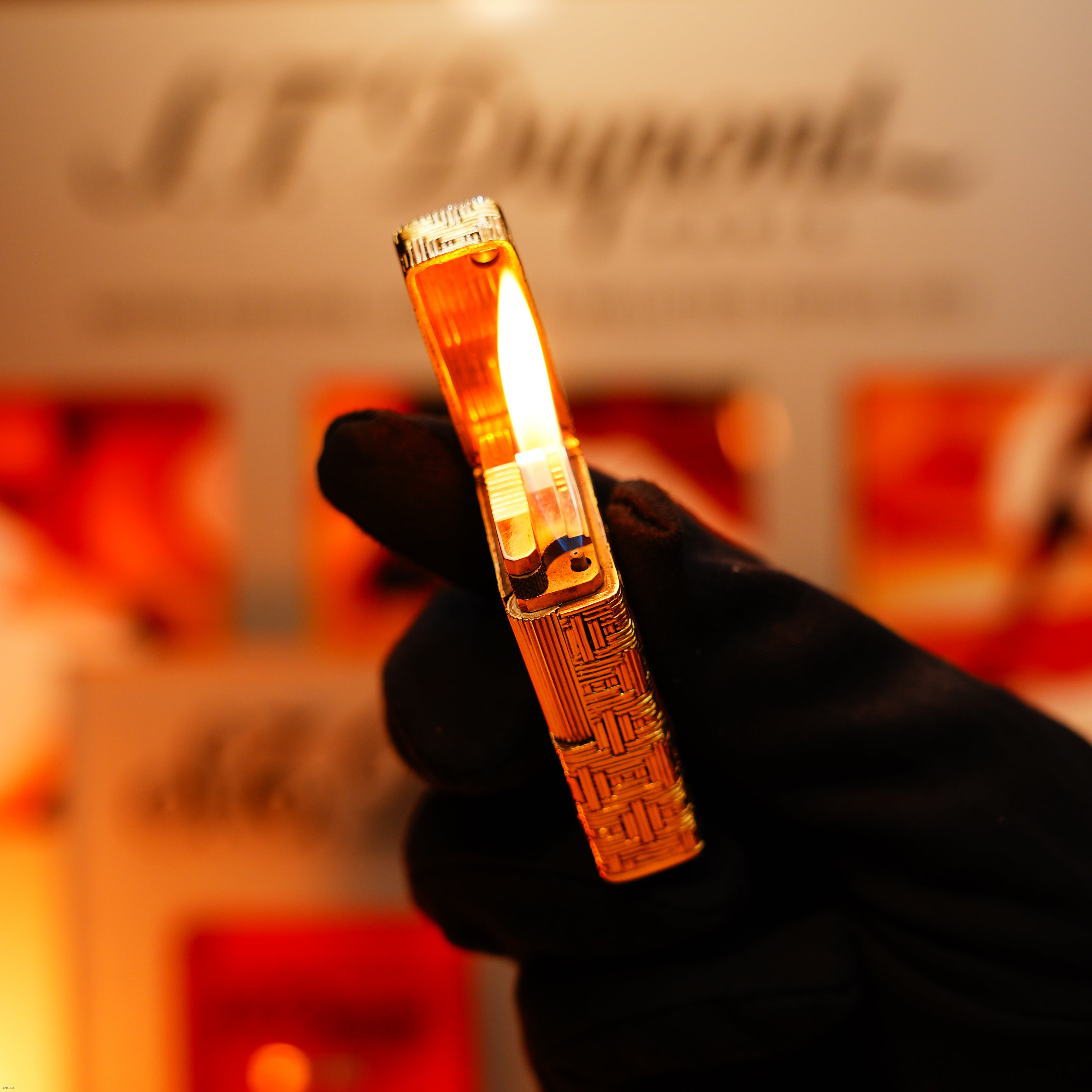 A gloved hand holds a Vintage 1960 Extremely Rare 1/1 St Dupont Lighter—Solid 18K Gold, Heavy Early Edition, 750 Hallmarked—by Lucy Lighter, open flame glowing against a softly blurred backdrop.