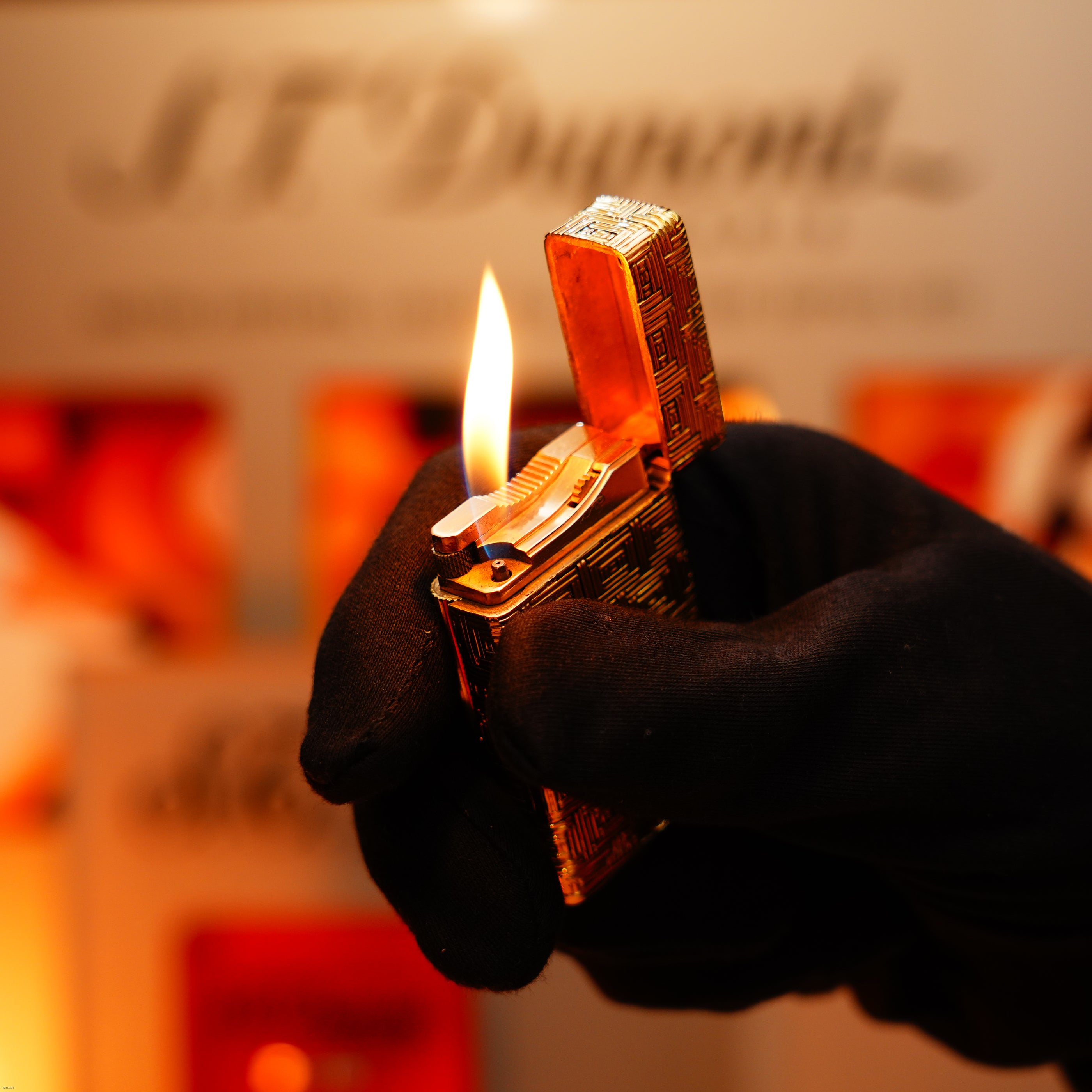 A gloved hand lights the Vintage 1960 Extremely Rare 1/1 St Dupont Lighter by Lucy Lighter—crafted from solid 18K gold, heavy early edition, with a 750 hallmark—as its gold pattern gleams and a visible flame flickers against a blurred background.