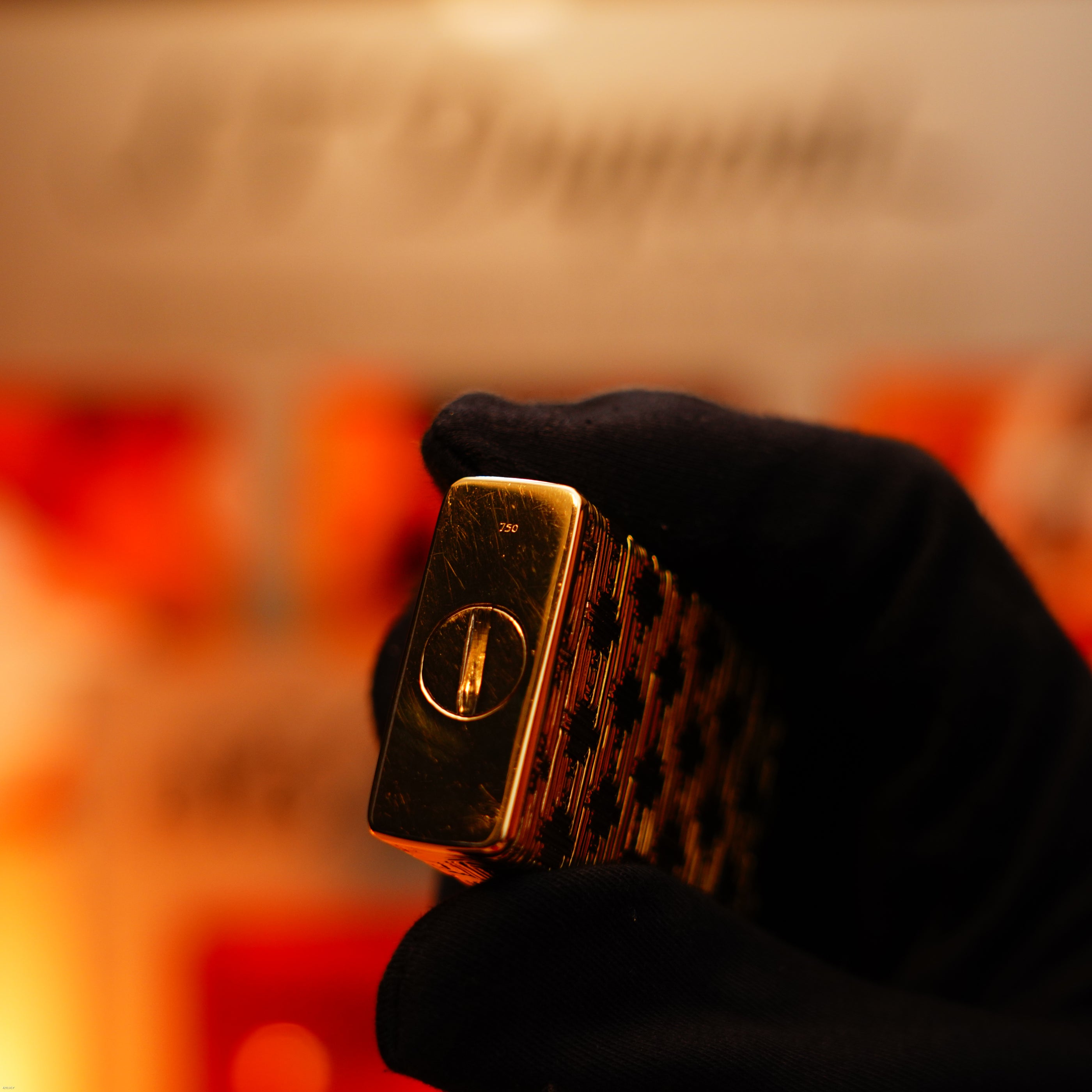 A gloved hand holds a Vintage 1960 Extremely Rare 1/1 Solid 18K Gold Lucy Lighter, heavy early edition with a 750 hallmark, its textured pattern gleaming as the brand name softly blurs in the background.