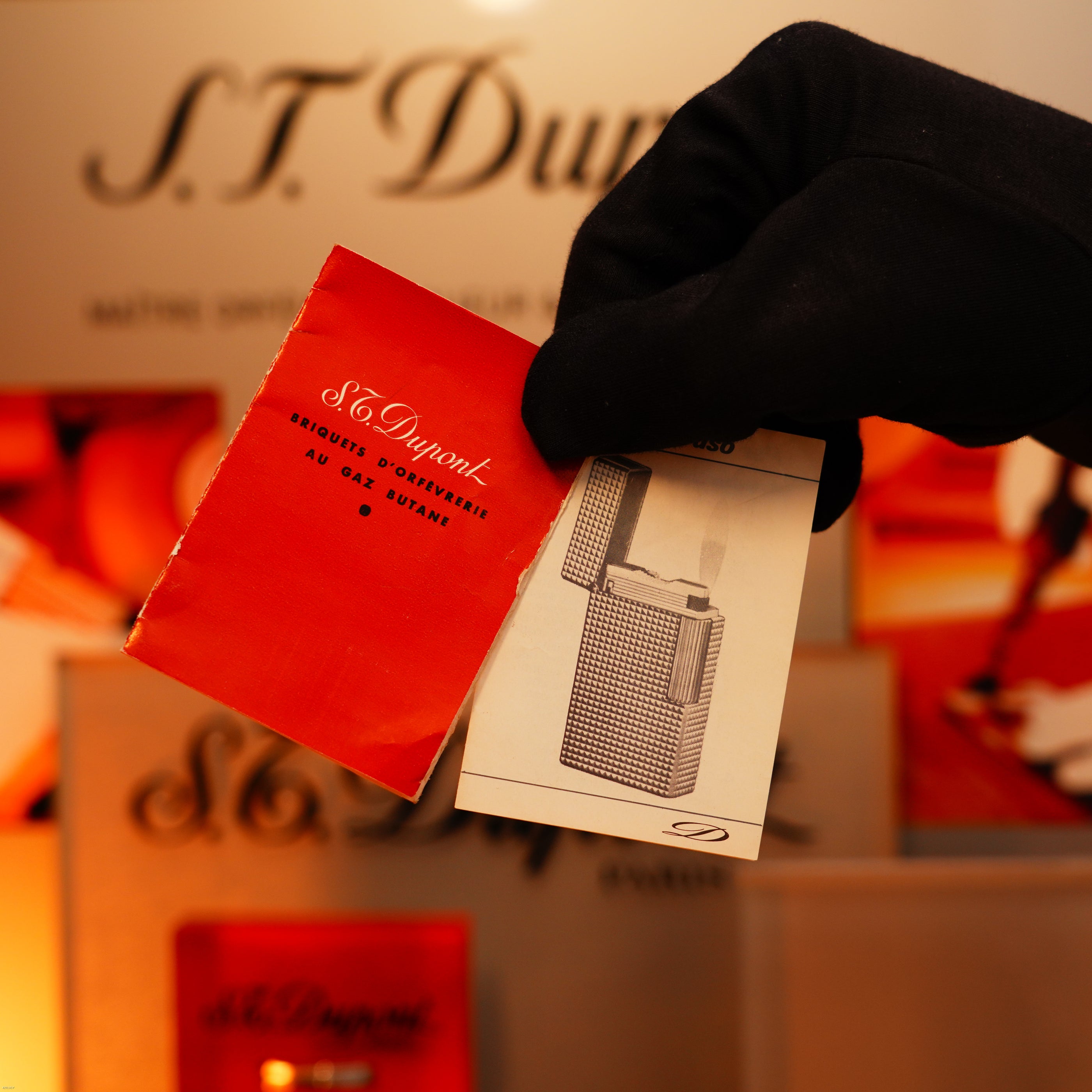 A gloved hand holds a red booklet and leaflet displaying the Vintage 1960 Extremely Rare 1/1 Lucy Lighter—Solid 18K Gold, Heavy Early Edition, 750 hallmarked—with branded packaging in the background.