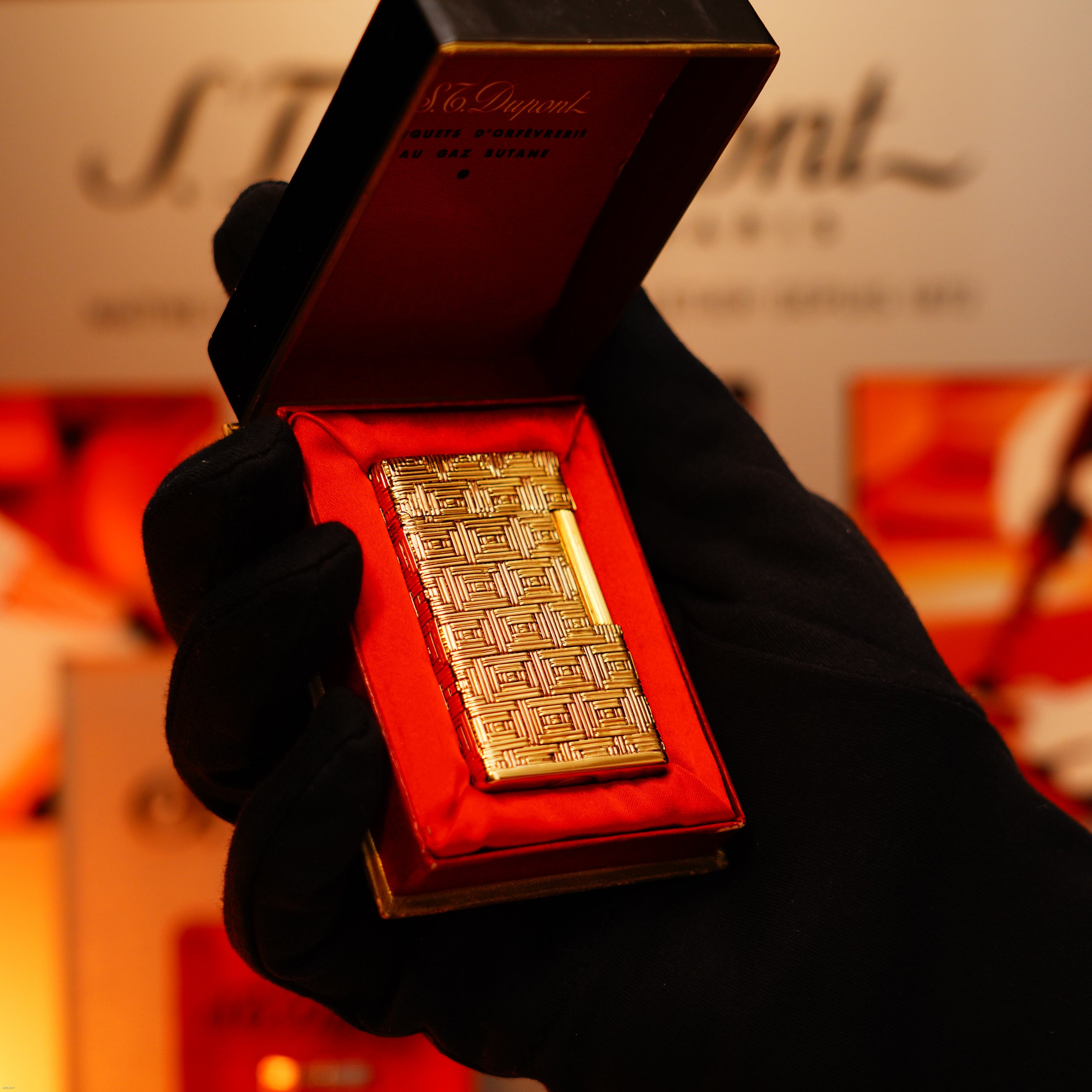 A gloved hand holds an open box displaying a Lucy Lighter: Vintage 1960 Extremely Rare 1/1 St Dupont Lighter, solid 18K gold, heavy early edition with 750 hallmark, set in red satin lining.