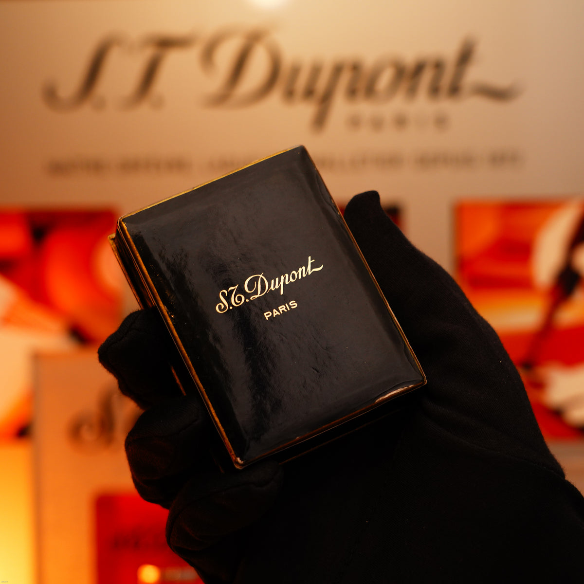 A gloved hand holds the Vintage 1960 Extremely Rare 1/1 Lucy Lighter—Solid 18K Gold, Heavy Early Edition, 750 Hallmarked—by Lucy Lighter, with a branded display softly blurred in the background.