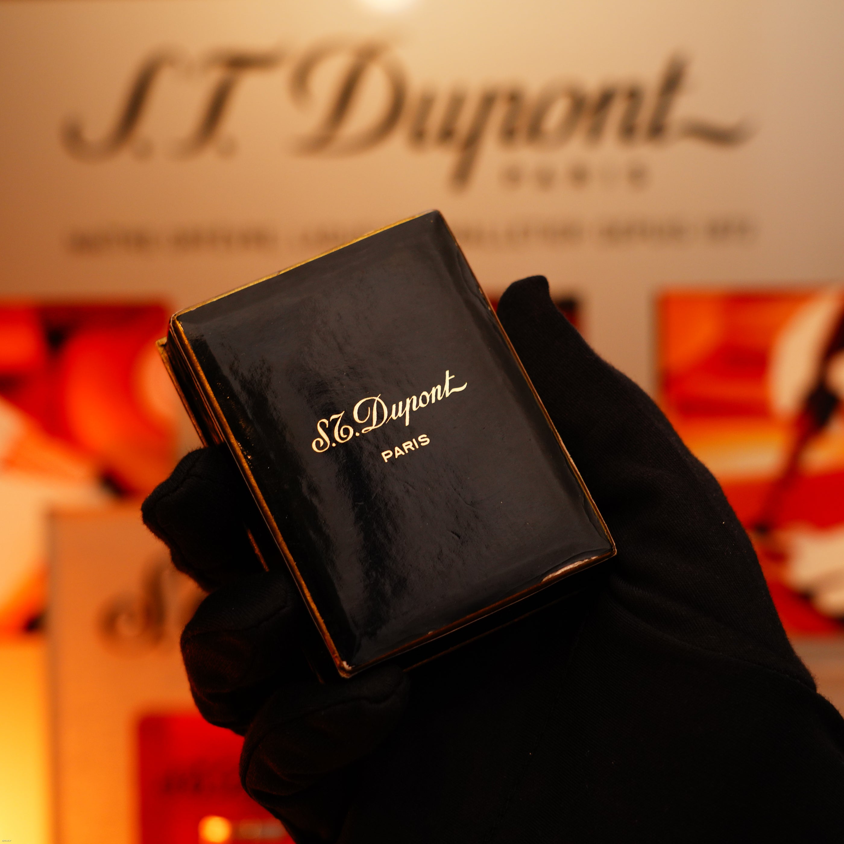 A gloved hand holds the Vintage 1960 Extremely Rare 1/1 Lucy Lighter—Solid 18K Gold, Heavy Early Edition, 750 Hallmarked—by Lucy Lighter, with a branded display softly blurred in the background.