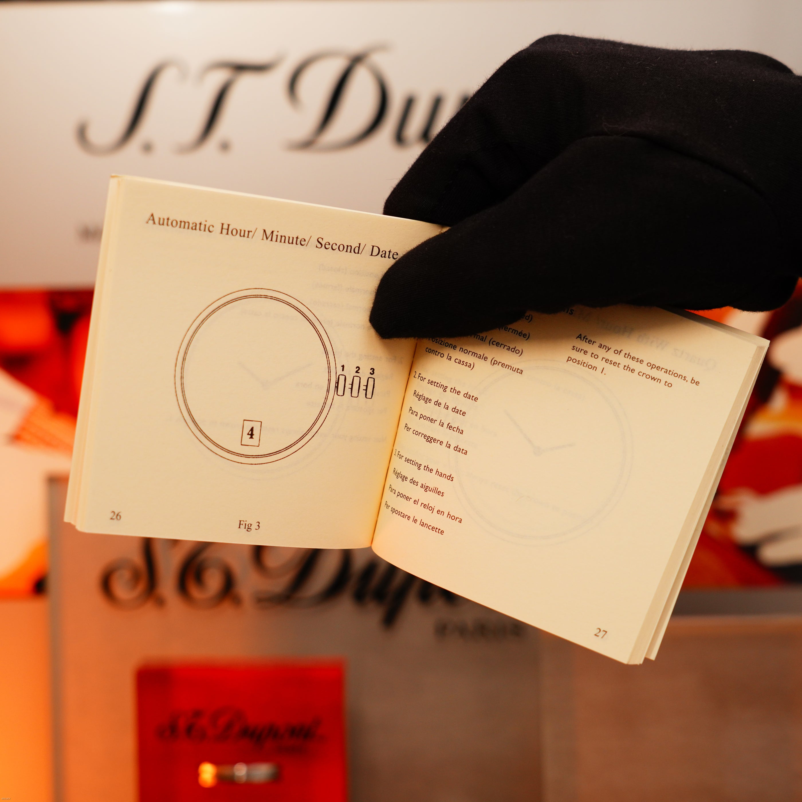 A gloved hand holds a small manual opened to pages showing diagrams and text about watch settings, with blurred Lucy Lighter branding and mention of the 12-month warranty beside the Vintage Extremely Rare Alfred Dunhill Full Set GMT.