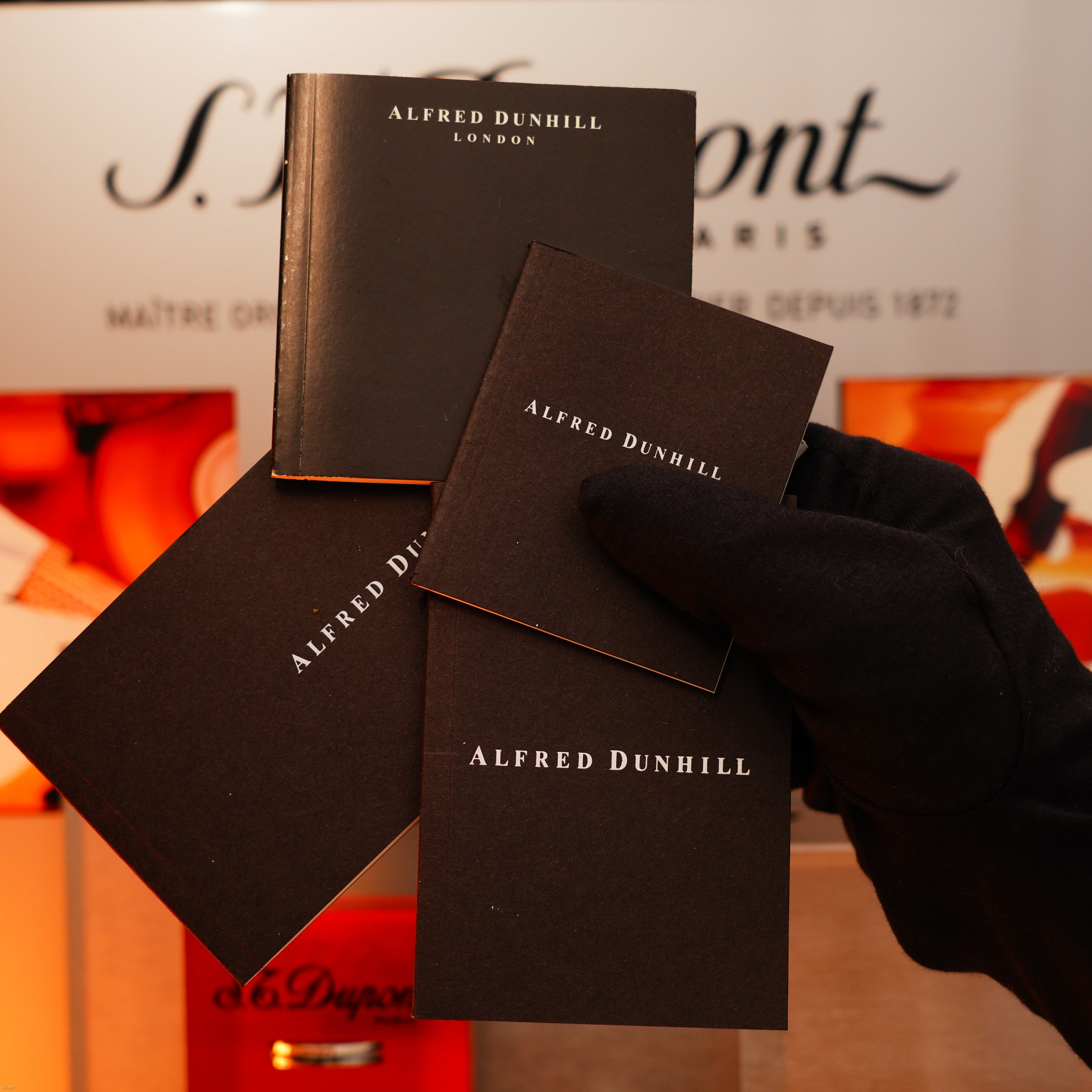 A gloved hand holds three Alfred Dunhill booklets, highlighting the quality of the Vintage Extremely Rare Alfred Dunhill Full Set GMT Full Solid Stainless Steel lighter by Lucy Lighter, with its signature full set packaging.