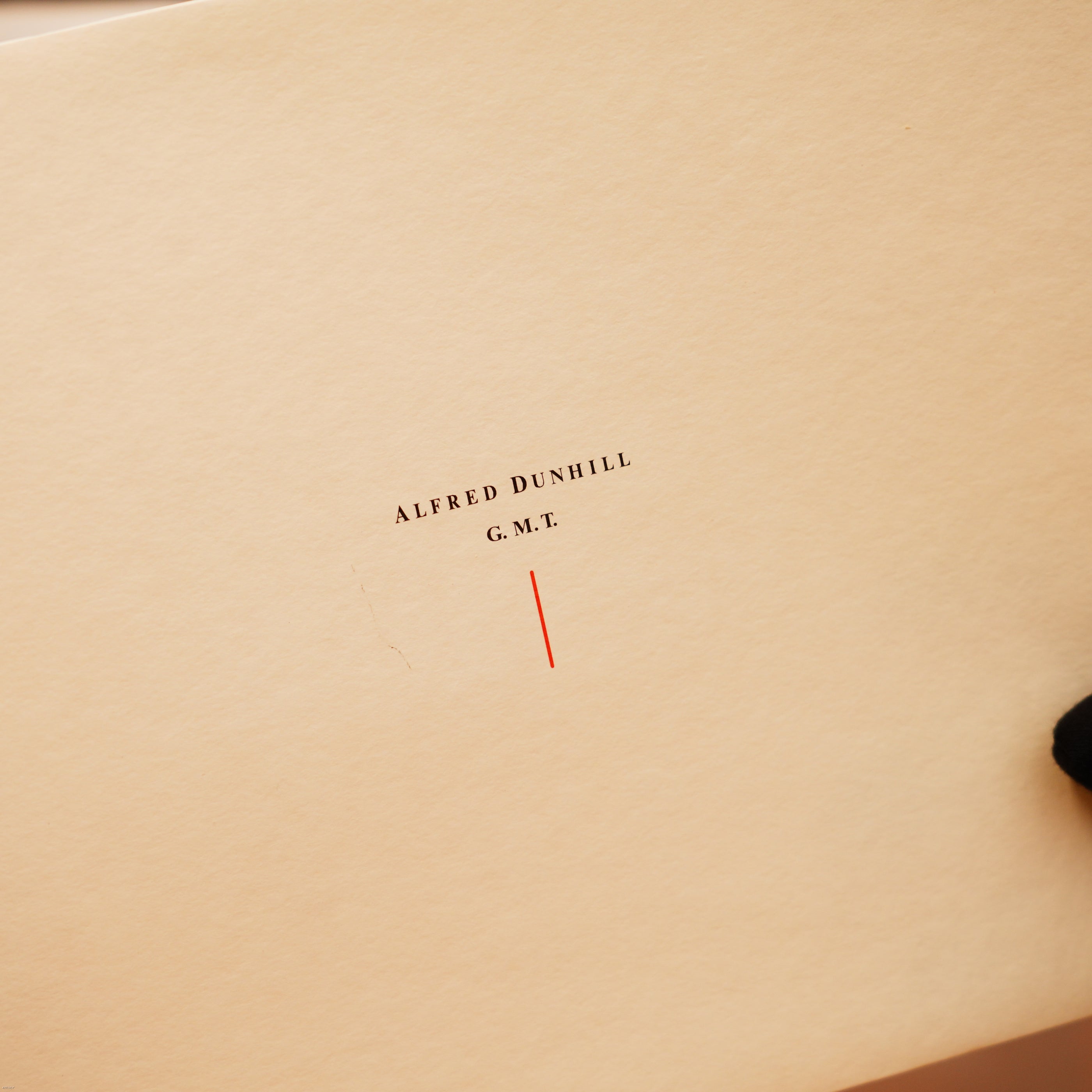 A hand in a black glove holds a cream card with “ALFRED DUNHILL G.M.T.” and a red line, symbolizing the quality guarantee of the Vintage Extremely Rare Lucy Lighter Alfred Dunhill Full Set GMT Solid Stainless Steel with signature.