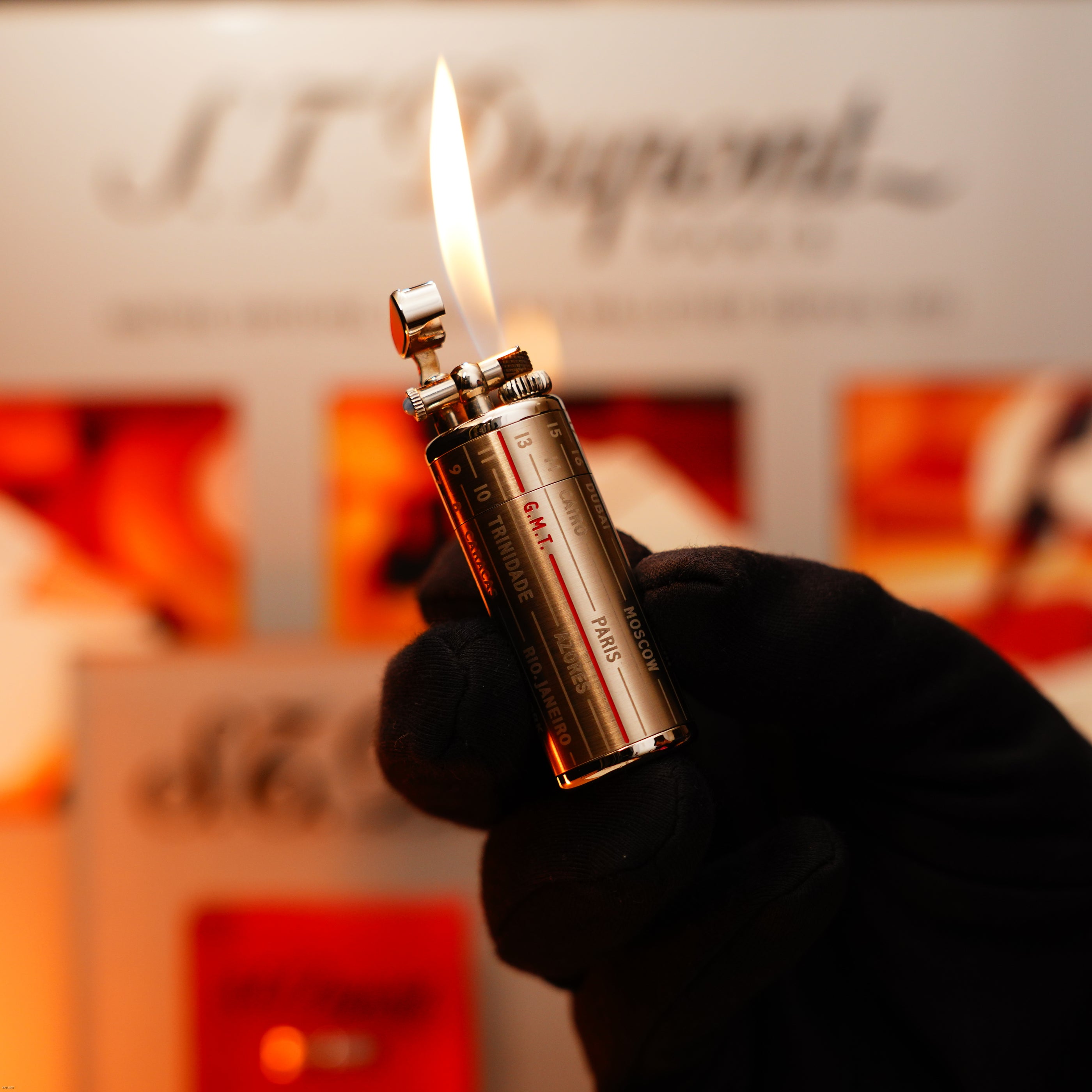 A gloved hand holds a lit Lucy Lighter Vintage Extremely Rare Alfred Dunhill Full Set GMT Solid Stainless Steel lighter, its flame aglow, with blurred packaging and mention of its 12-month warranty in the background.