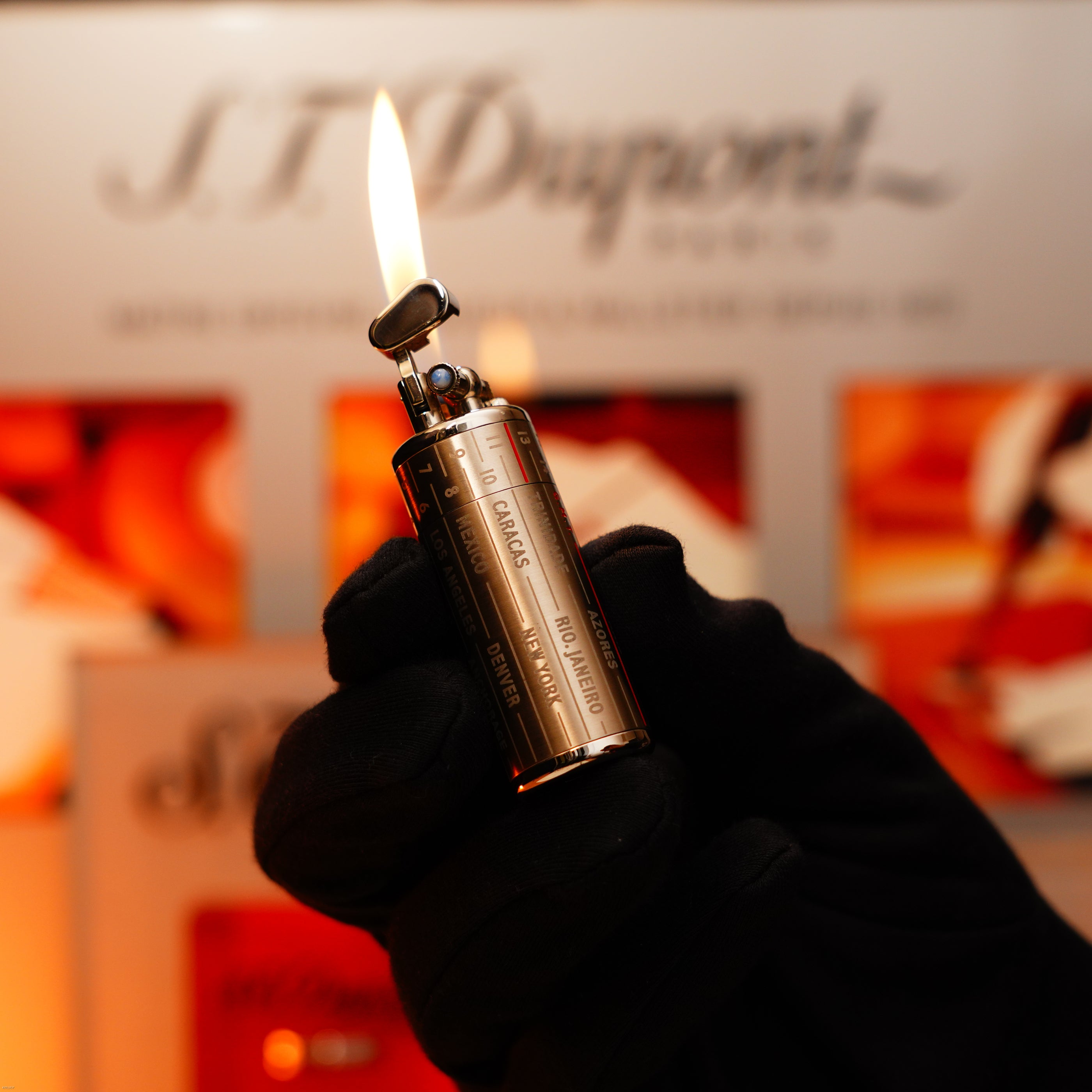 A gloved hand holds a lit Lucy Lighter Vintage Extremely Rare Alfred Dunhill Full Set GMT in solid stainless steel, with visible flame and Alfred Dunhill signature against a blurred background.