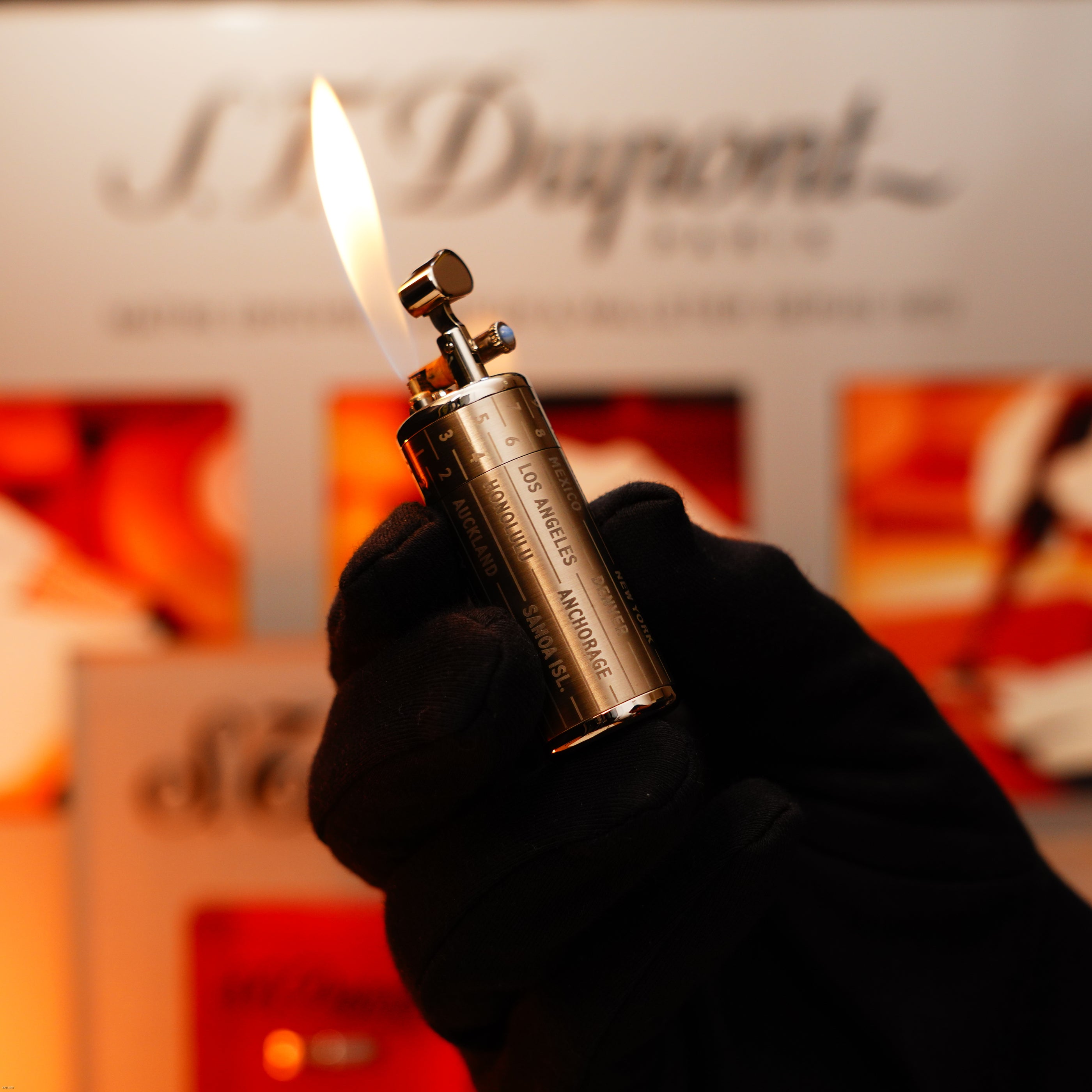 A gloved hand holds a Vintage Extremely Rare Alfred Dunhill Full Set GMT Full Solid Stainless Steel lighter by Lucy Lighter, its flame visible against a blurred background with the brand’s logo.