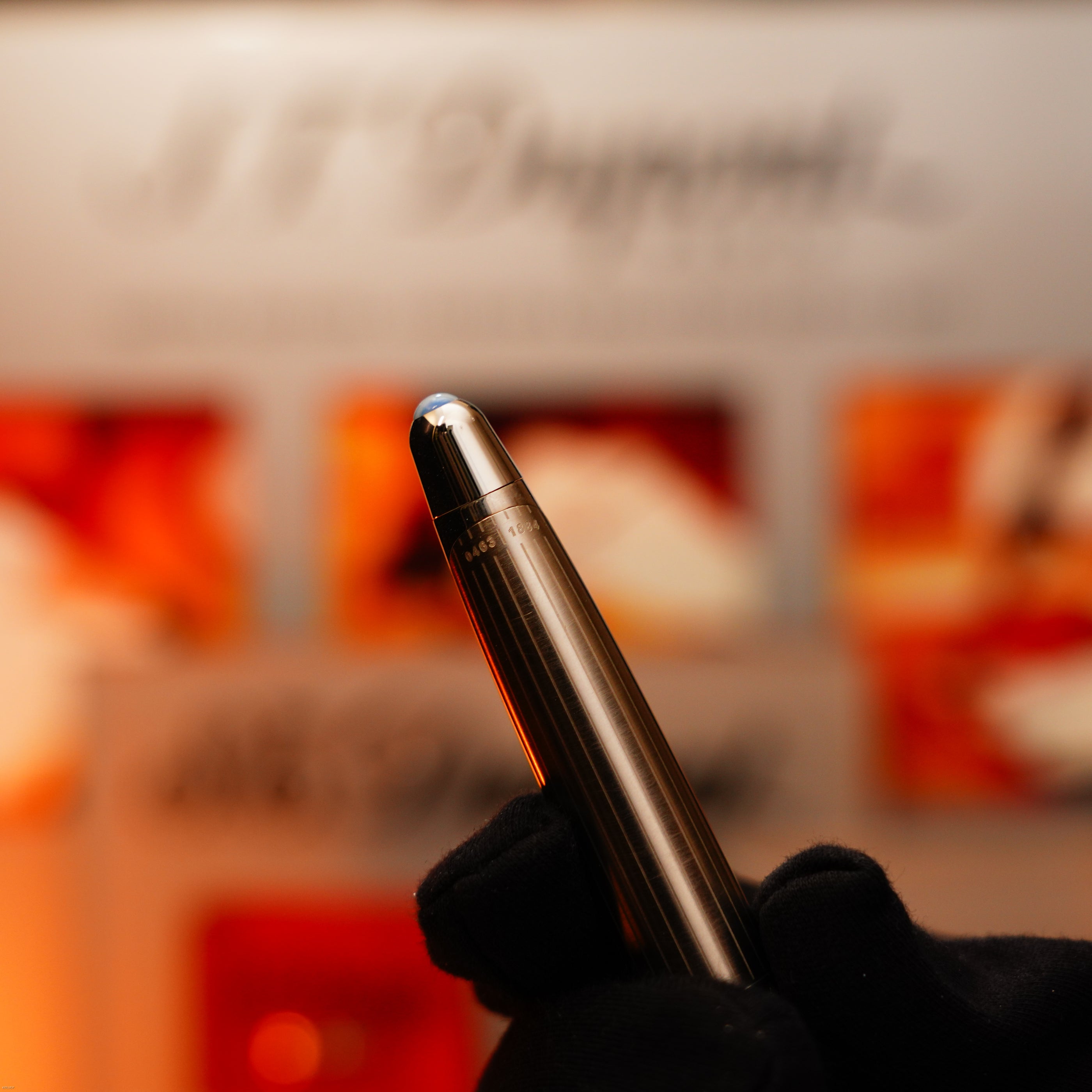 A gloved hand holds a metallic pen with a rounded tip against a blurred background featuring the Lucy Lighter brand and the Vintage Extremely Rare Alfred Dunhill Full Set GMT Full Solid Stainless Steel with Alfred Dunhill Signature.