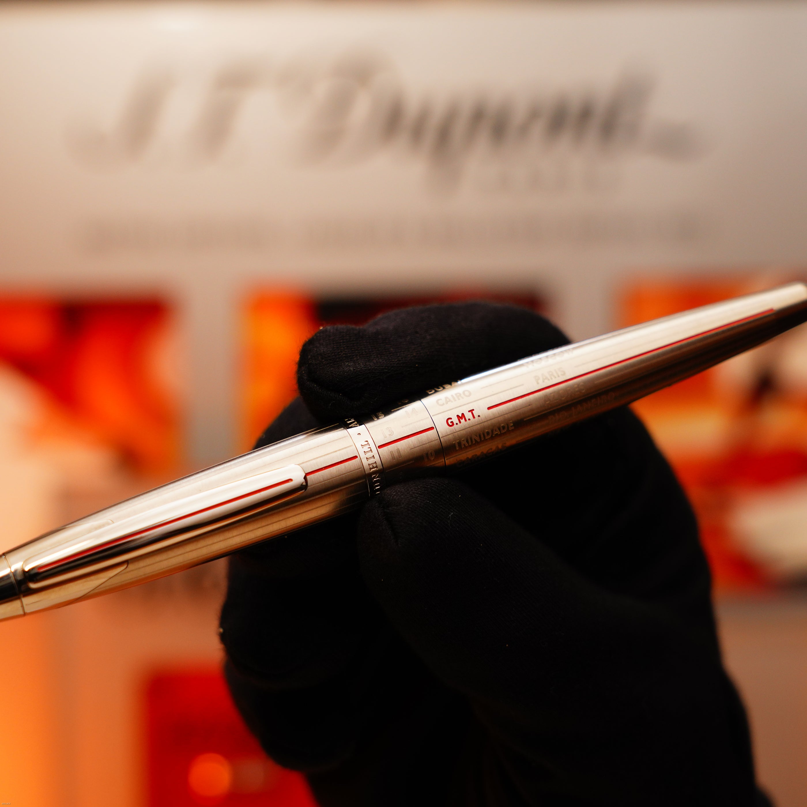 A gloved hand holds a Vintage Extremely Rare Alfred Dunhill Full Set GMT Solid Stainless Steel watch with Alfred Dunhill Signature, by Lucy Lighter, against a blurred display—a symbol of superior craftsmanship and exclusivity.