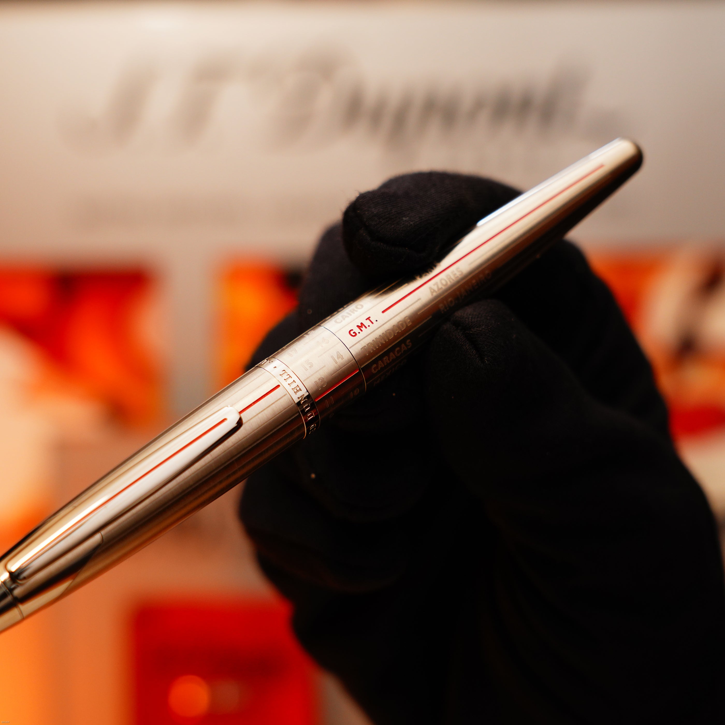 A gloved hand holds a solid stainless steel Vintage Extremely Rare Alfred Dunhill Full Set GMT by Lucy Lighter, featuring the Alfred Dunhill signature and exuding the elegance of classic luxury, set against a blurred background.