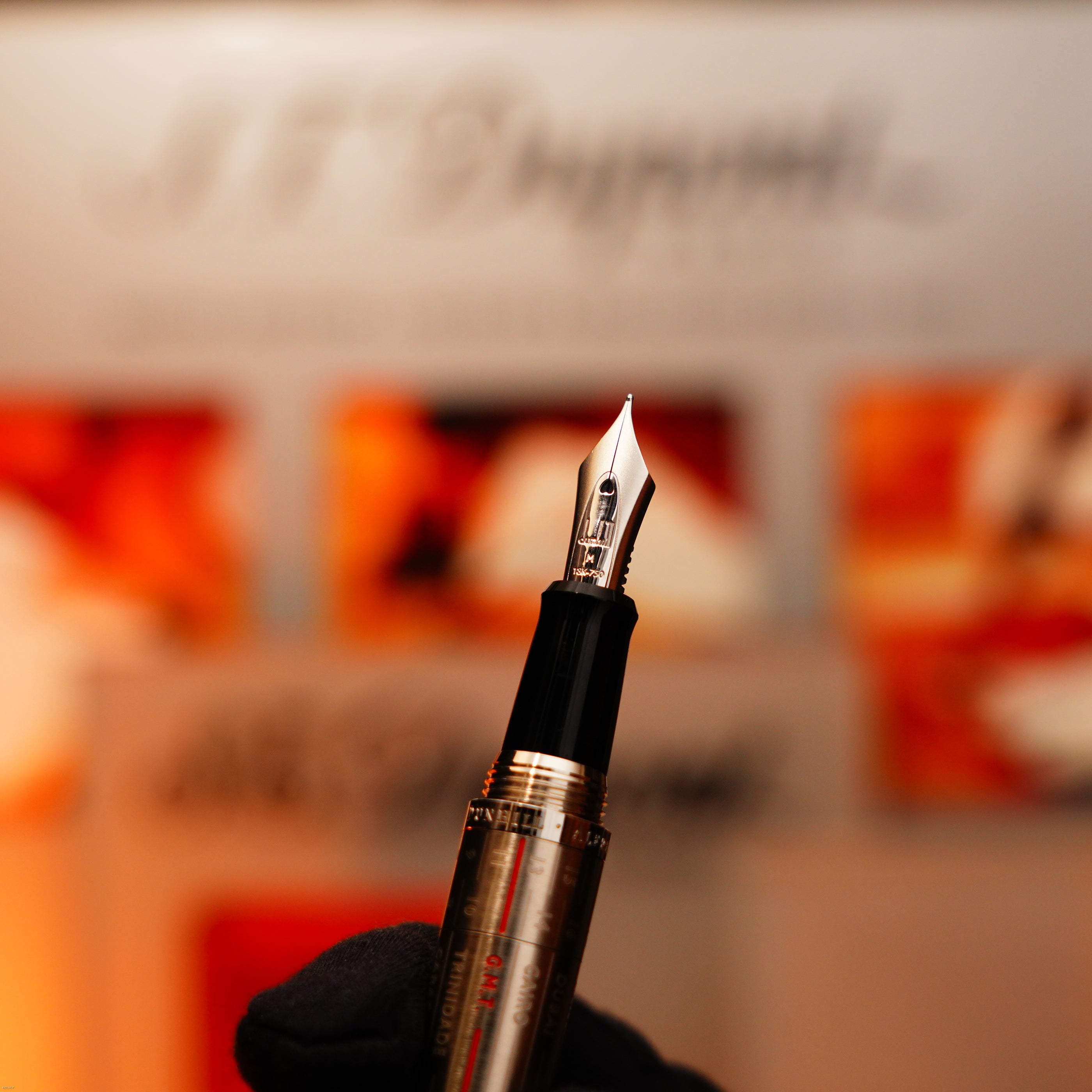 A gloved hand holds the Vintage Extremely Rare Alfred Dunhill Full Set GMT Solid Stainless Steel by Lucy Lighter, its refined details against a blurred orange and white backdrop evoke luxury craftsmanship and assure premium quality.