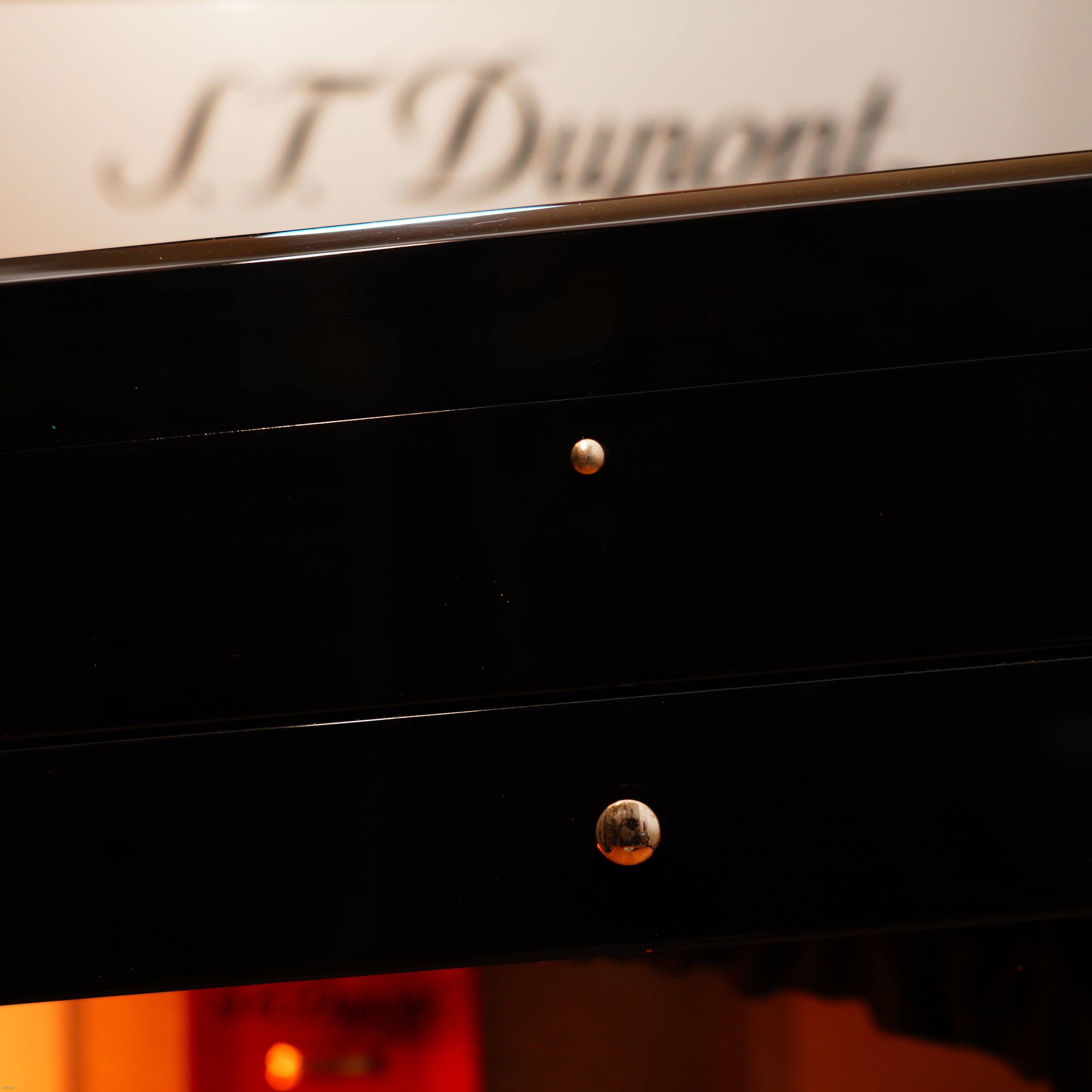 Close-up of a glossy black drawer with two round metallic knobs; blurred "Lucy Lighter" text evokes the timeless elegance of the Vintage Extremely Rare Alfred Dunhill GMT Full Solid Stainless Steel Full Set.