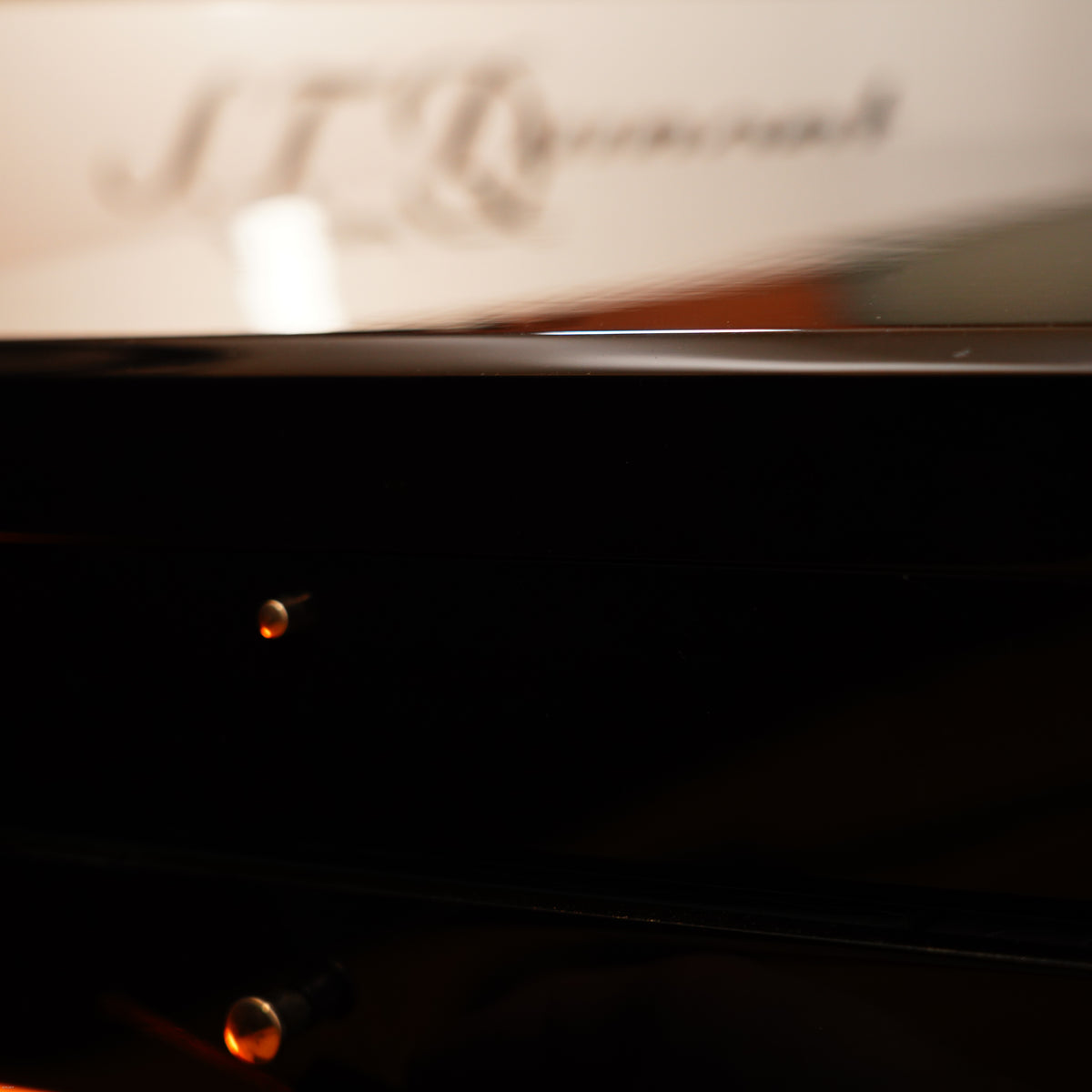 Close-up of a glossy black piano with blurred "Lucy Lighter" branding reflected on the surface, reminiscent of the Vintage Extremely Rare Alfred Dunhill Full Set GMT Solid Stainless Steel lighter with signature full set.