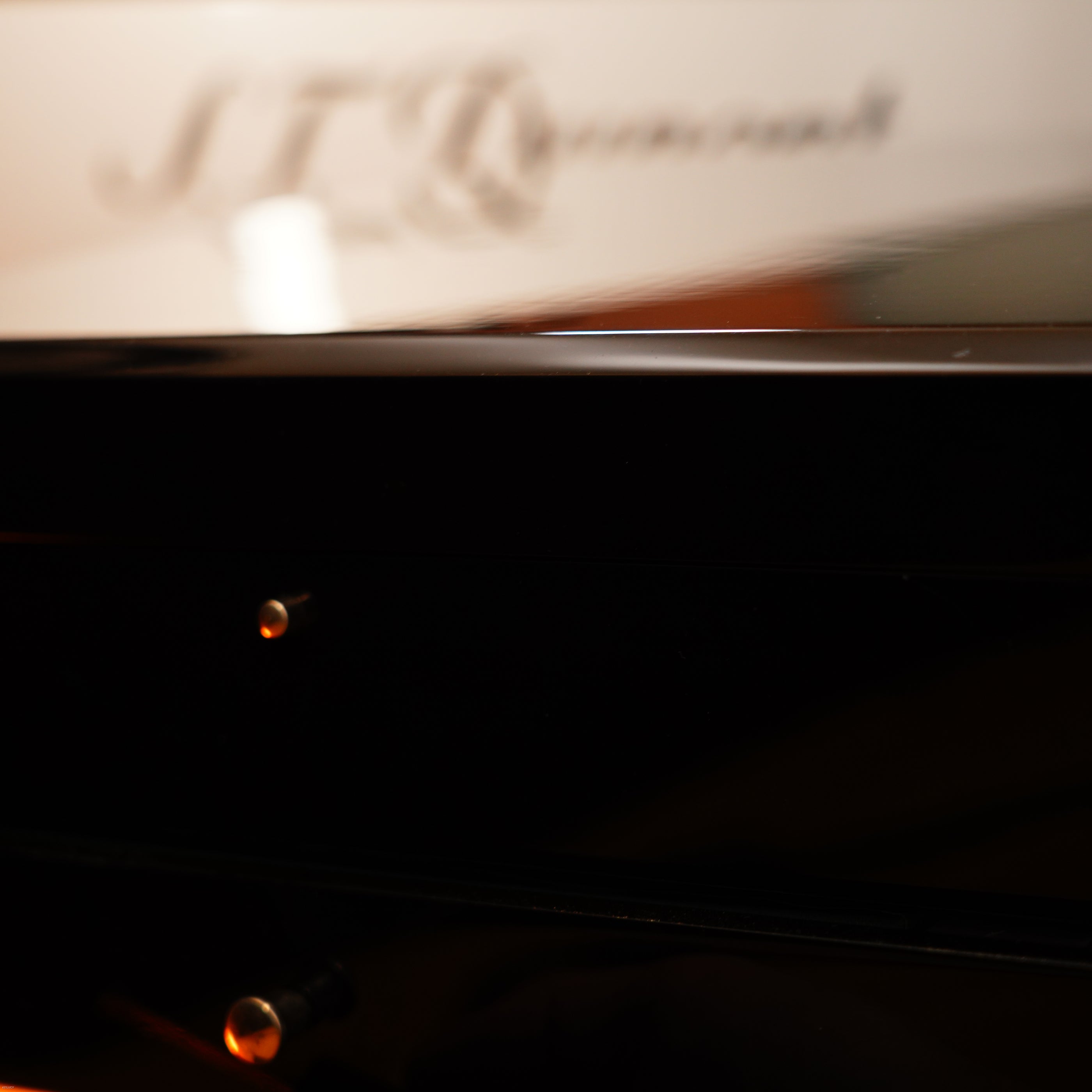 Close-up of a glossy black piano with blurred "Lucy Lighter" branding reflected on the surface, reminiscent of the Vintage Extremely Rare Alfred Dunhill Full Set GMT Solid Stainless Steel lighter with signature full set.