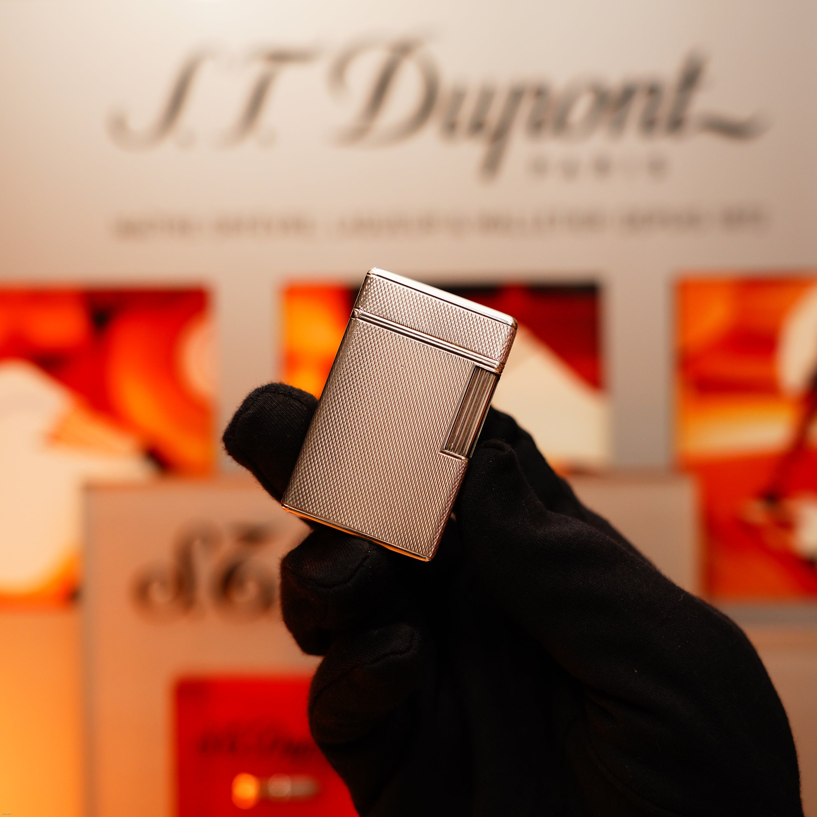 A gloved hand holds the Vintage 1970 Extremely Rare 1/1 De St Dupont Solid 925 Sterling Ligne 1 Heavy Barley Pattern Lighter by Lucy Lighter, displayed before a blurred backdrop, highlighting unique craftsmanship and timeless style.