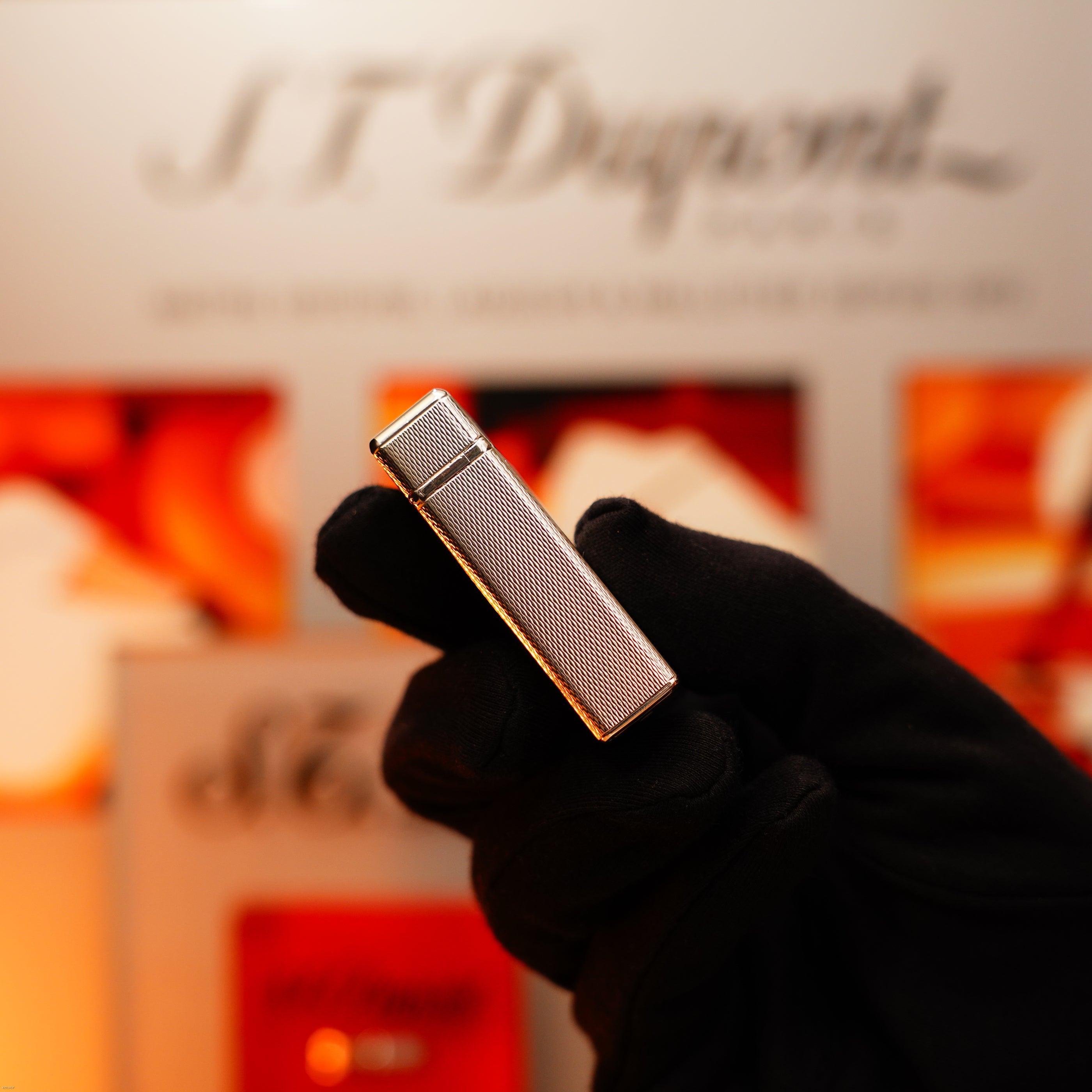 A gloved hand holds up a Vintage 1970 Extremely Rare 1/1 De St Dupont Solid 925 Sterling Ligne 1 Heavy Barley Pattern Lighter by Lucy Lighter with a textured silver surface, against a blurred background.