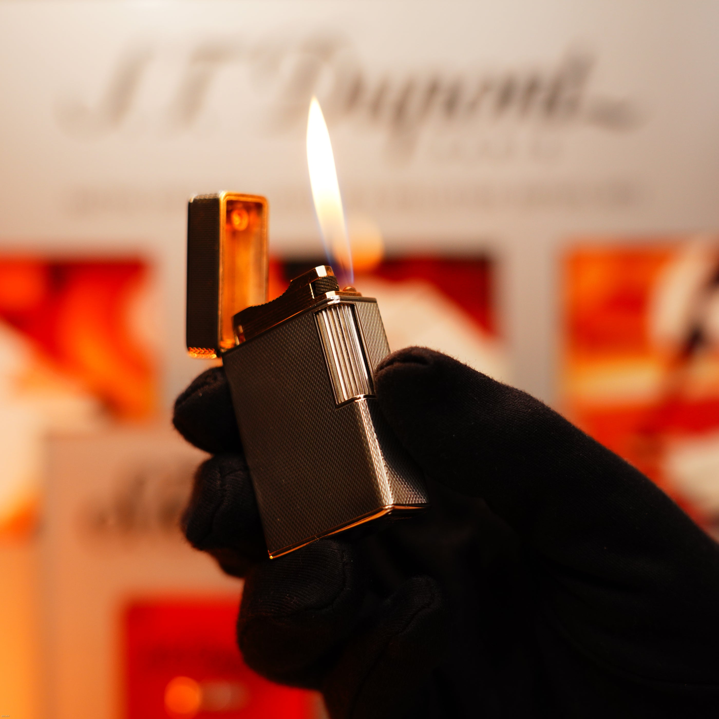 A gloved hand holds an open, lit Lucy Lighter Vintage 1970 Extremely Rare 1/1 De St Dupont Solid 925 Sterling Ligne 1 Heavy Barley Pattern Lighter with visible flame against a blurred background.