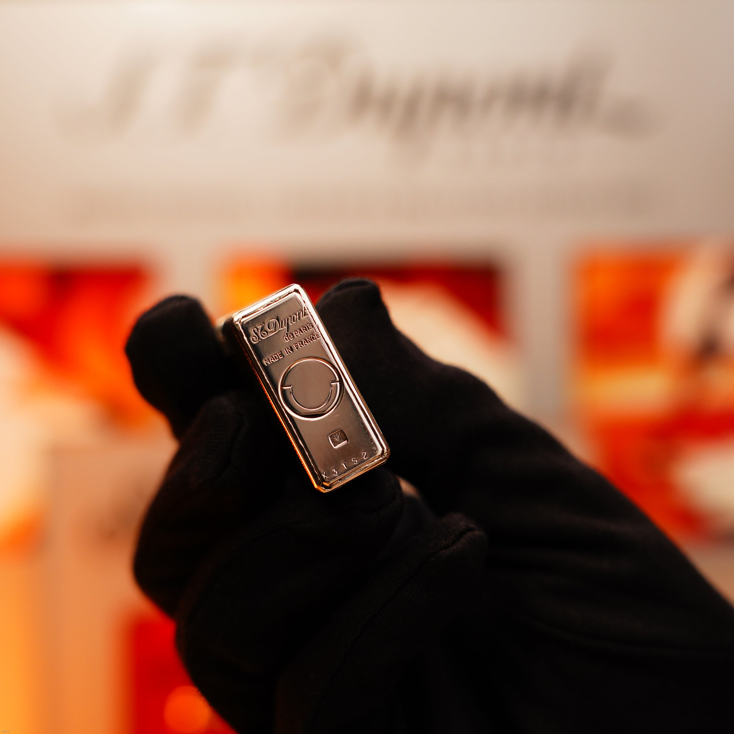 A gloved hand holds the Vintage 1970 Extremely Rare 1/1 De St Dupont Solid 925 Sterling Rare Ligne 1 Heavy Barley Pattern Lighter by Lucy Lighter upright, showcasing timeless elegance and rarity against a blurred background.