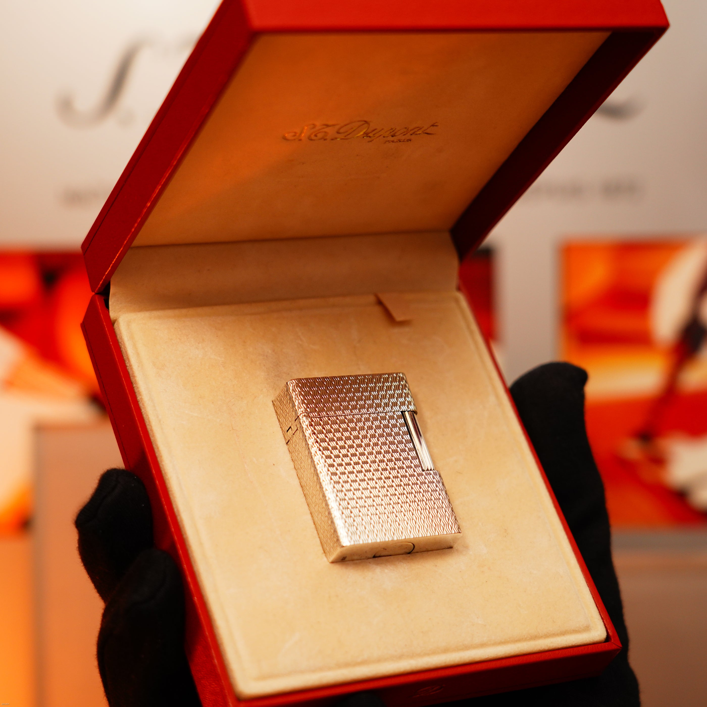 A gloved hand holds an open red box showcasing the Lucy Lighter Vintage 1970 Extremely Rare 1/1 De St Dupont Solid 925 Sterling Ligne 1 Heavy Guilloché Pattern Lighter on a cream cushion.