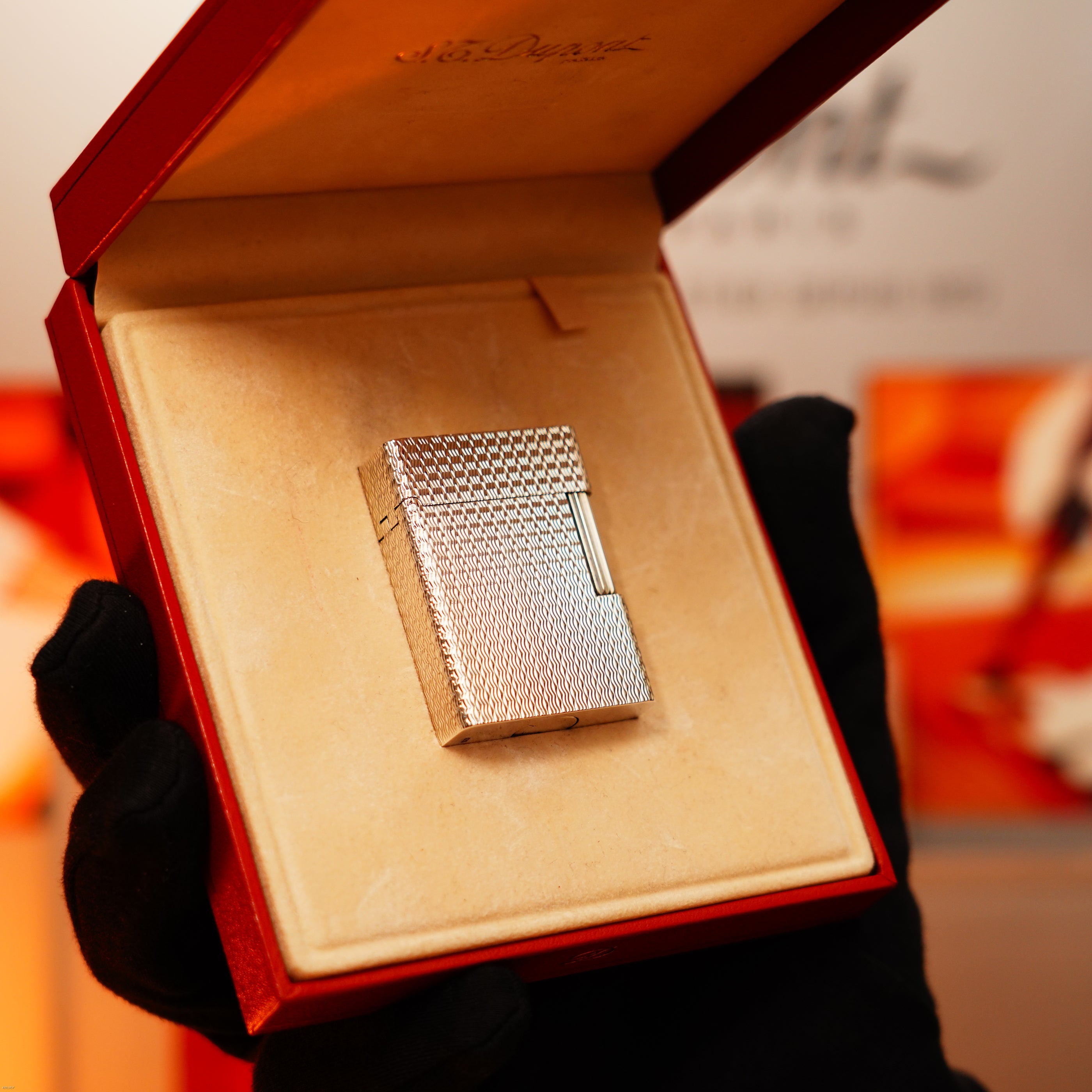 A gloved hand holds an open red box displaying a Vintage 1970 Extremely Rare 1/1 De St Dupont Solid 925 Sterling Ligne 1 Heavy Guilloché Pattern Lighter by Lucy Lighter, set on a beige cushion with a quality guarantee and 12-month warranty.