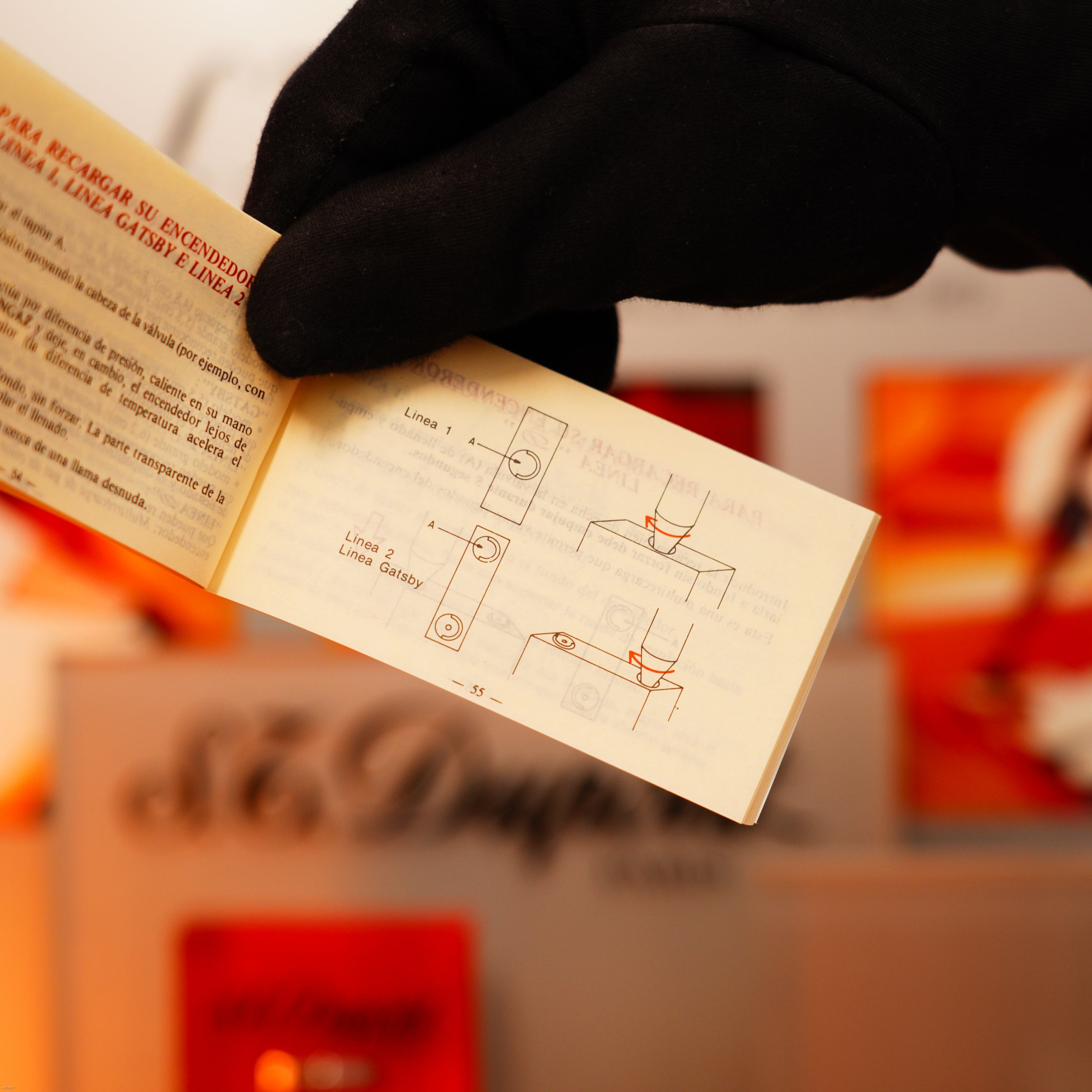 A gloved hand holds open a Spanish instruction booklet, with blurred vintage Lucy Lighter packaging and a quality guarantee in the background beside the Vintage 1970 Extremely Rare De St Dupont Solid 925 Sterling Ligne 1 Guilloché Lighter.