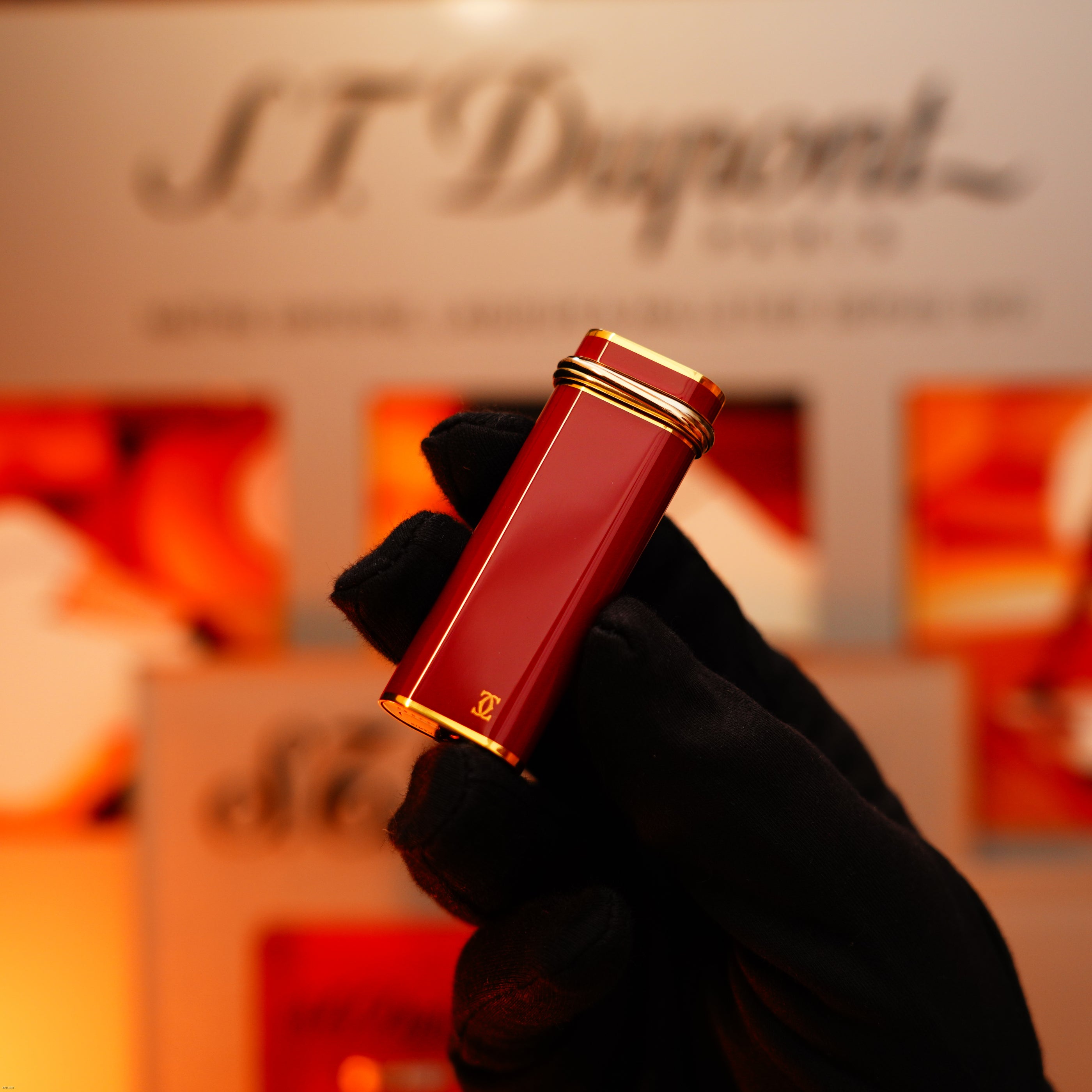 A gloved hand holds a Vintage 1970 Early Cartier Production Heavy Silver Finish Rare Guilloché Pattern Lighter by Lucy Lighter, with the brand's logo visible in the blurred background.