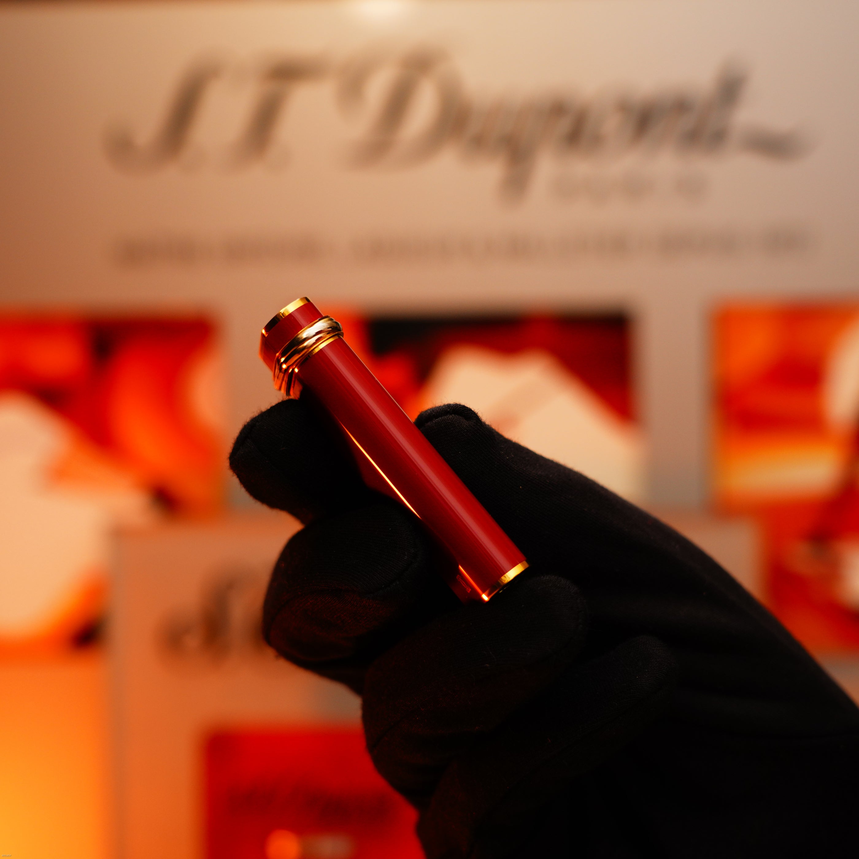 A gloved hand holds the Vintage 1980 Cartier Early Oval Le Must Lighter by Lucy Lighter—red passion lacquer, 24k gold finish, and iconic Trinity ring gleaming against a blurred background hinting at vintage Cartier luxury.