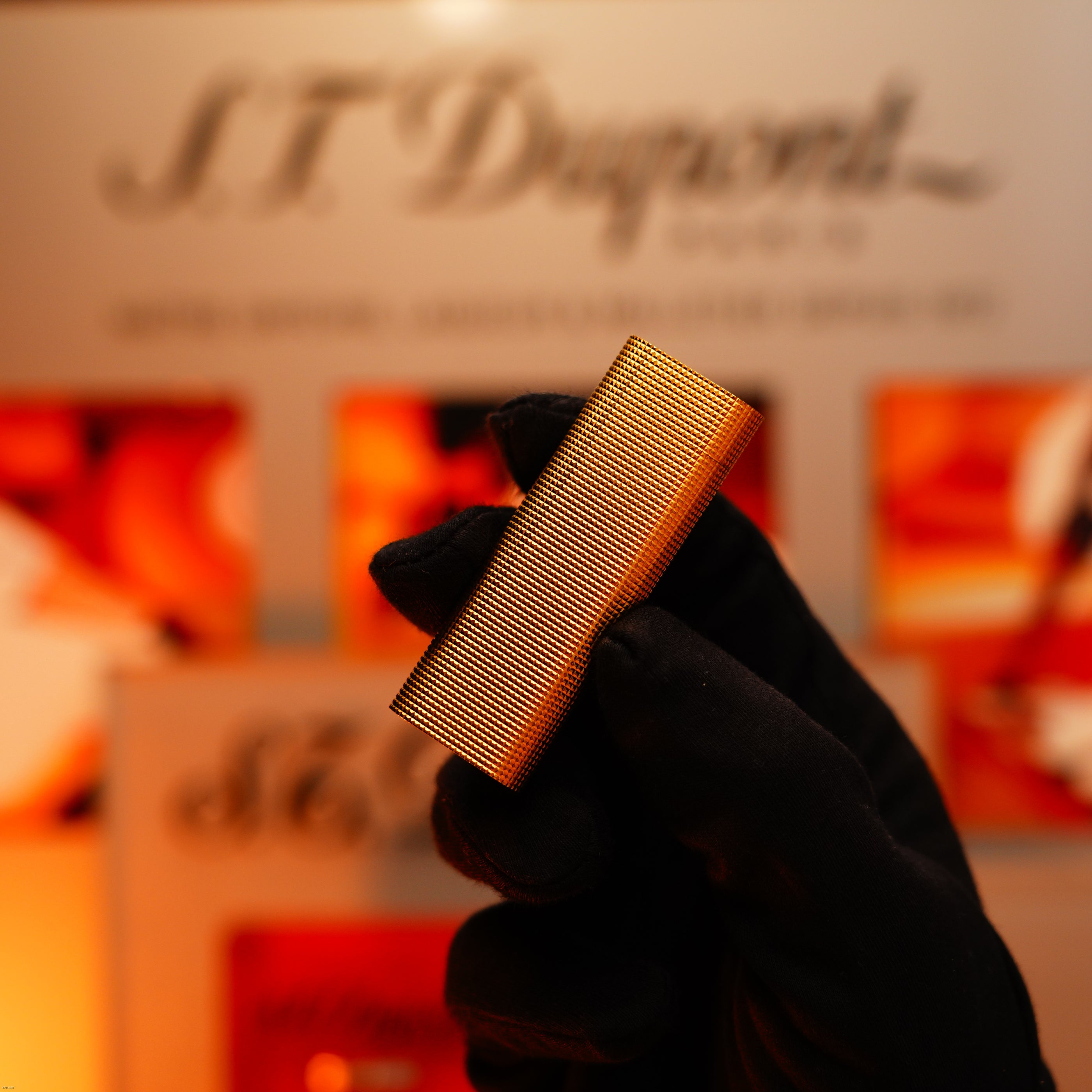 A gloved hand holds a Vintage 1970 Early Cartier Production Heavy Silver Finish Rare Guilloché Pattern Lighter by Lucy Lighter—a textured rectangular piece—in front of a blurred Lucy Lighter branded background.