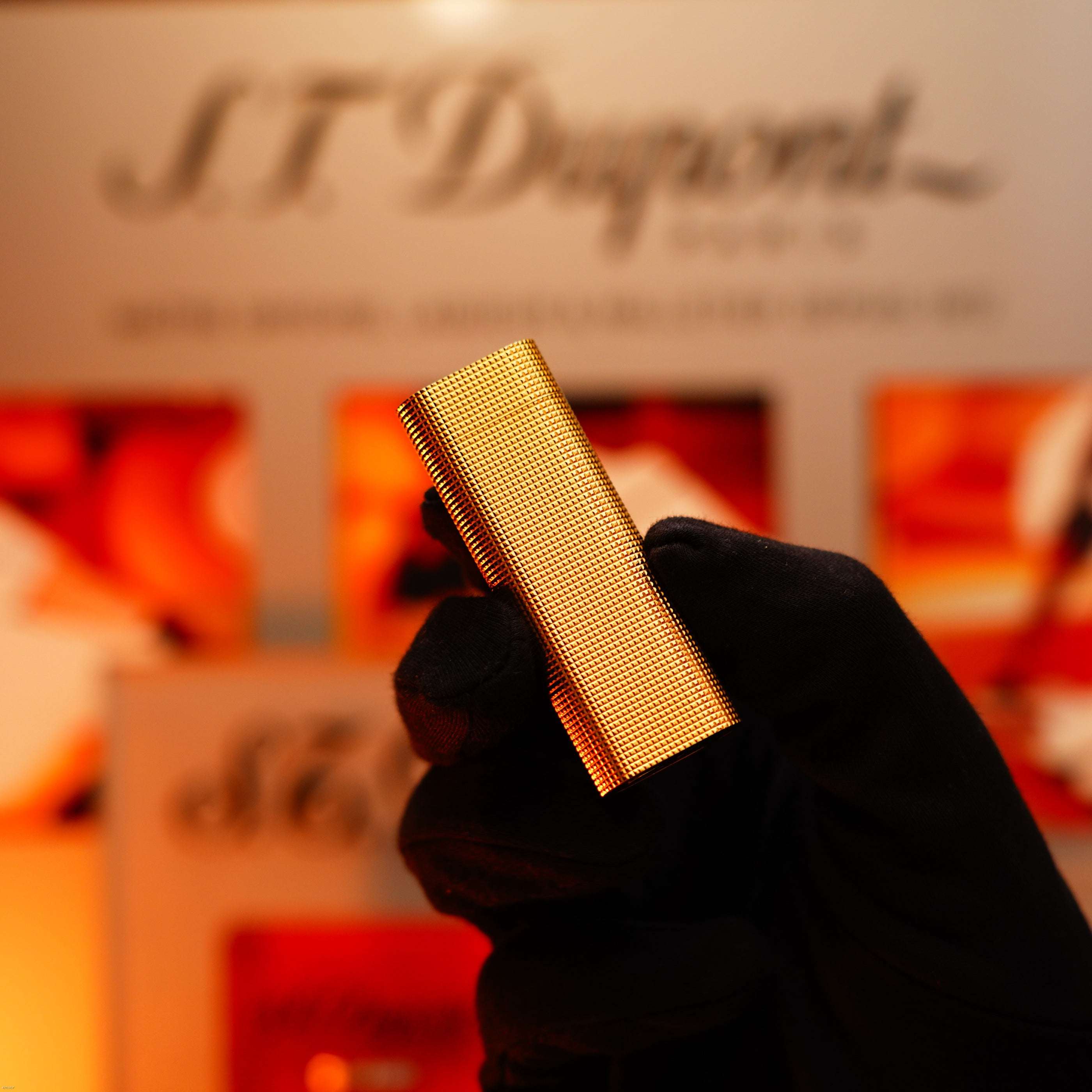 A gloved hand holds a Vintage 1970 Early Cartier Production Heavy Silver Finish Rare Guilloché Pattern Lighter by Lucy Lighter in front of a blurred branded display.