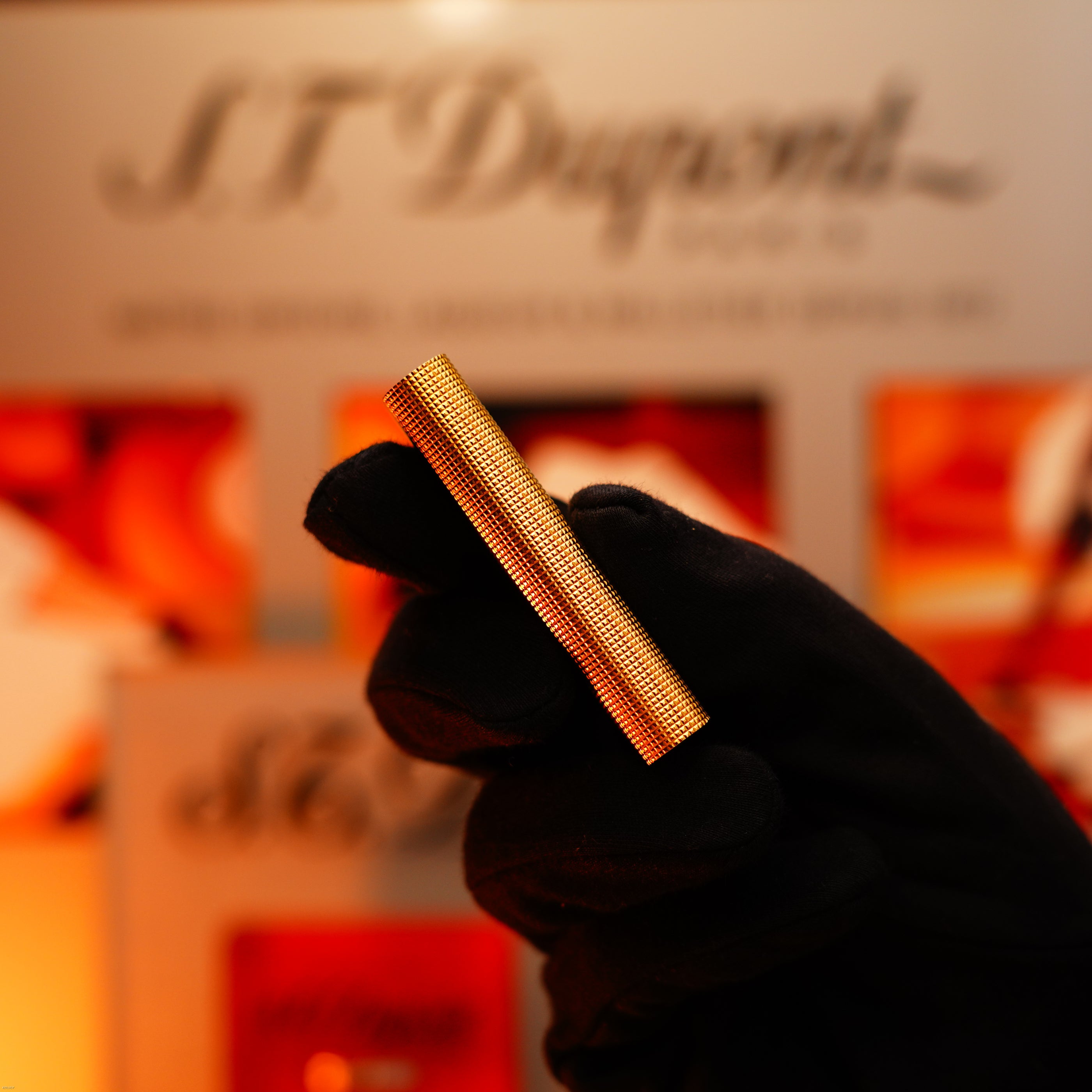 A gloved hand holds a Vintage 1970 Early Cartier Production Heavy Silver Finish Rare Guilloché Pattern Lighter by Lucy Lighter in front of a blurred display.