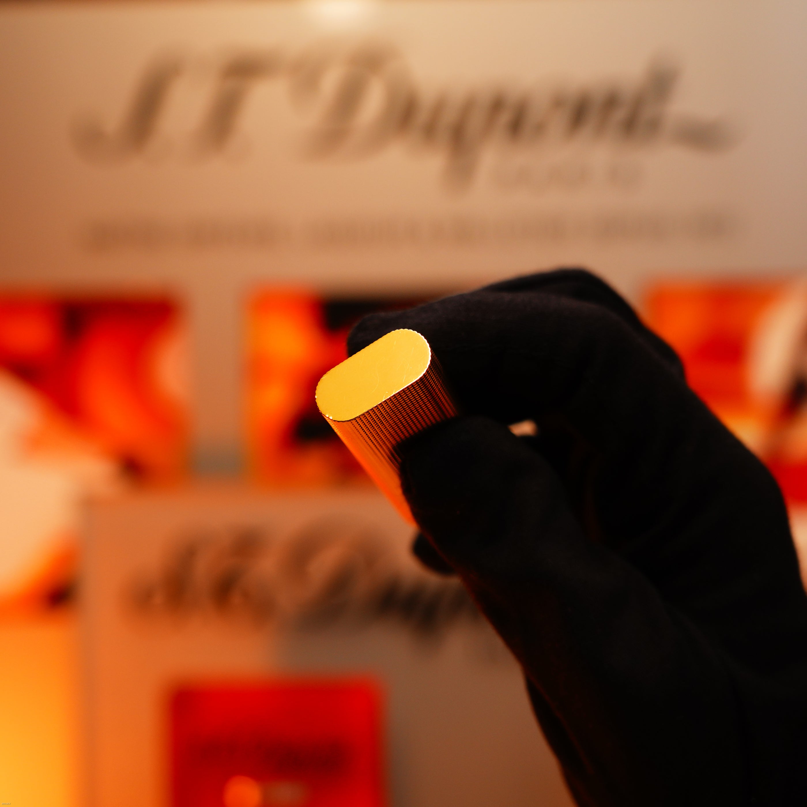 A gloved hand holds a small, silver-finished Lucy Lighter with a rare Guilloché pattern, evoking the design of a Vintage 1970 Early Cartier production, with blurred branding visible in the background.