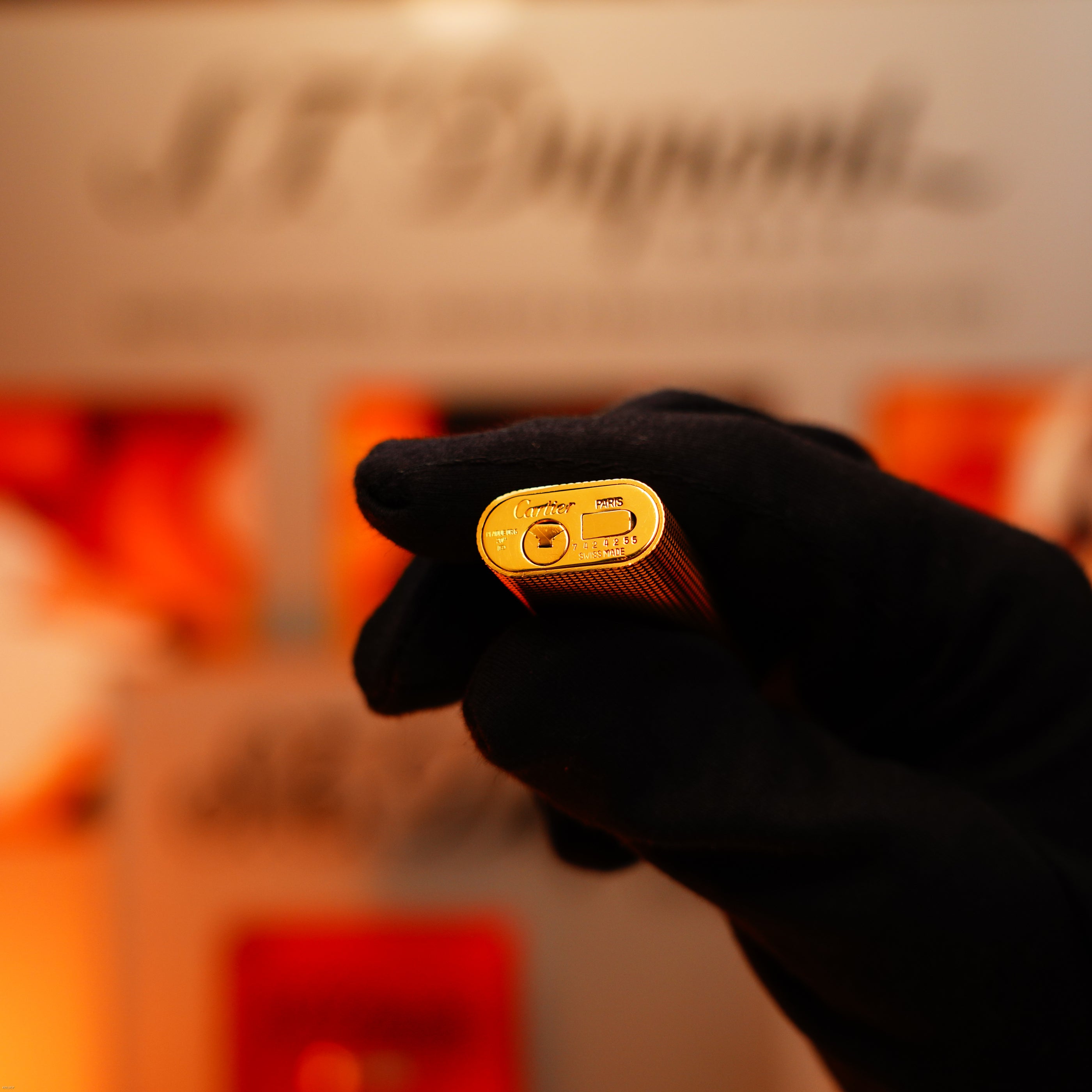 A gloved hand holds a Lucy Lighter Vintage 1970 Early Cartier Production Heavy Silver Finish Rare Guilloché Pattern Lighter, displaying the base with engraved branding and refill port.