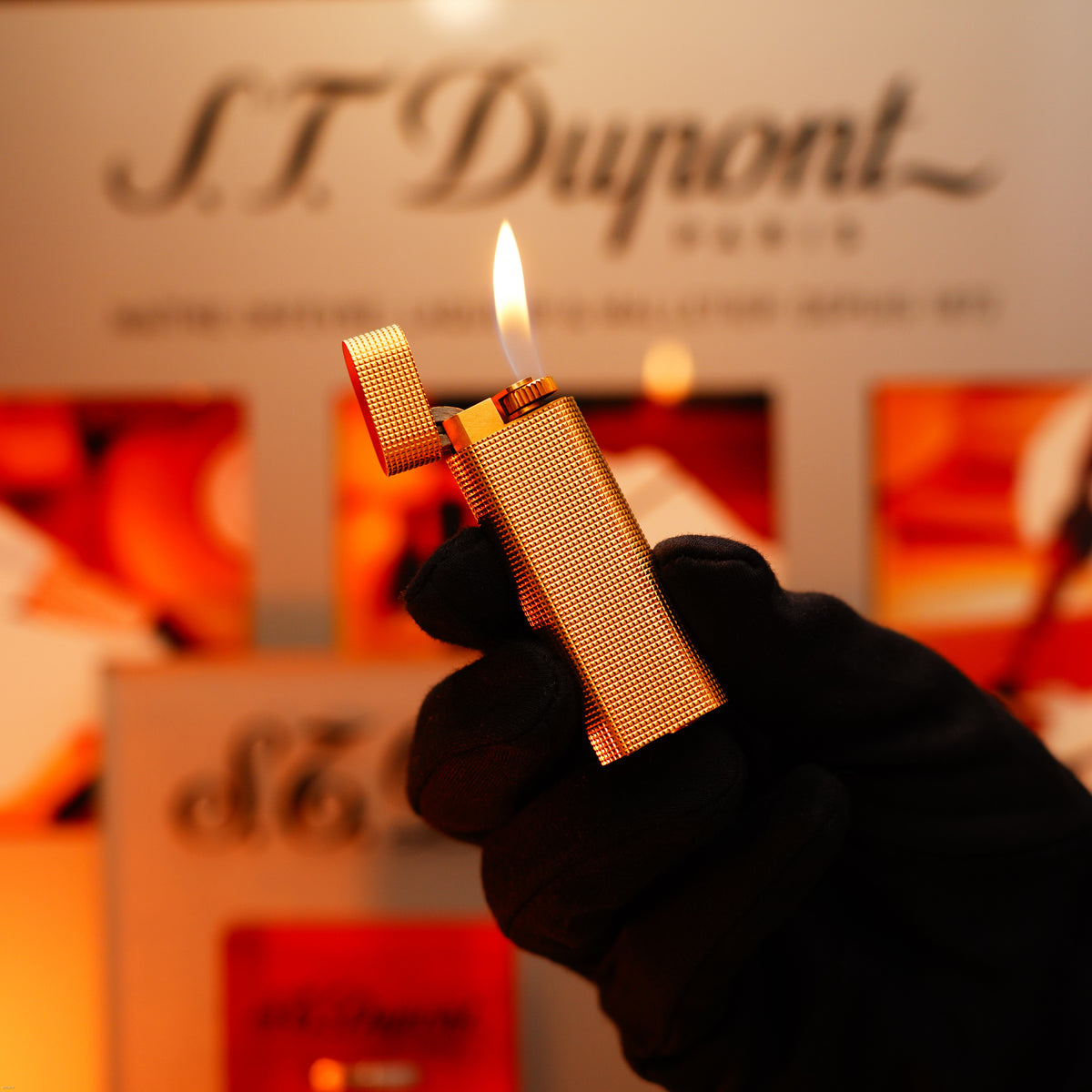 A gloved hand holds a lit Vintage 1970 Early Cartier Production Heavy Silver Finish Rare Guilloché Pattern Lighter by Lucy Lighter, with its flame glowing against a blurred background.