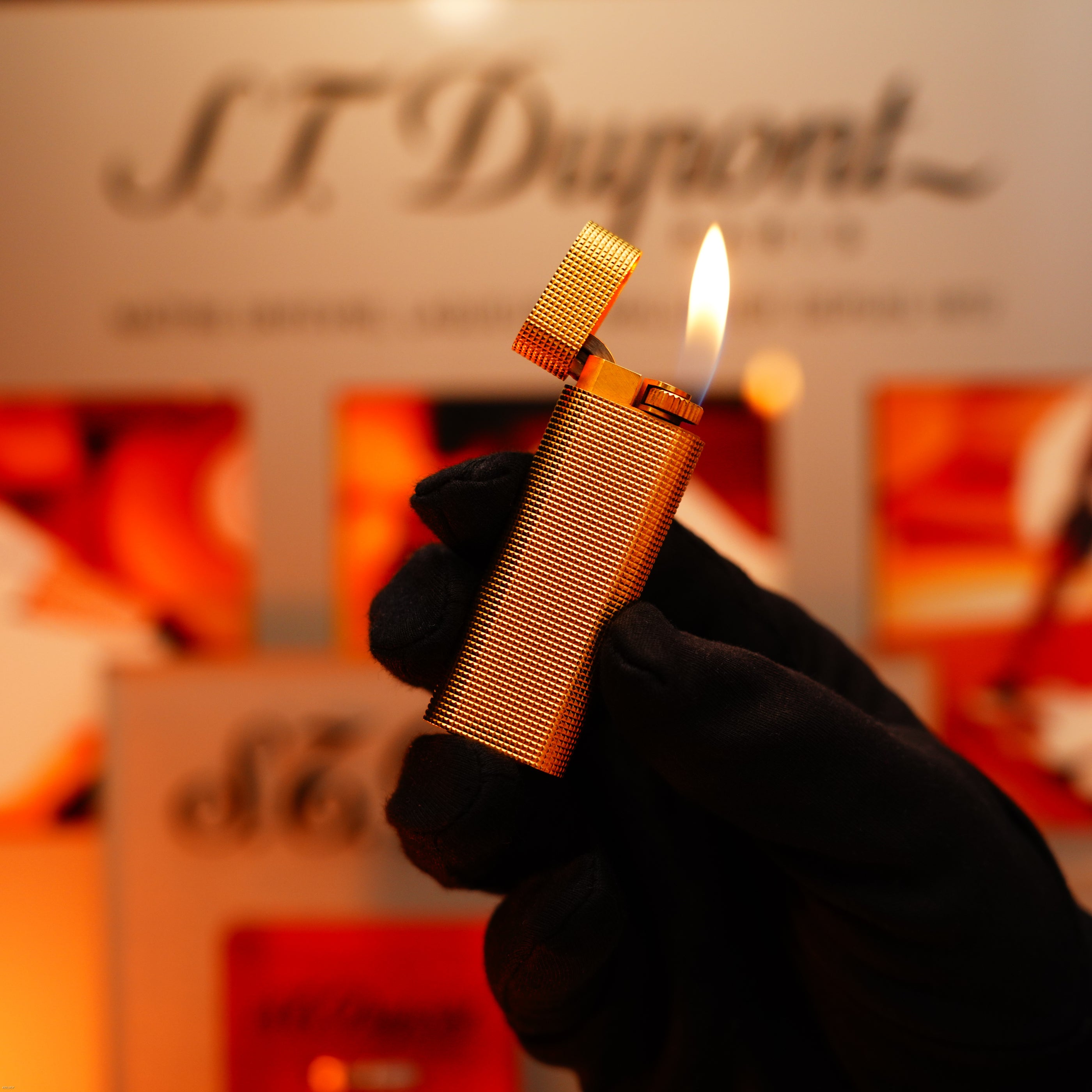 A gloved hand holds a lit Vintage 1970 Early Cartier Production Heavy Silver Finish Rare Guilloché Pattern Lighter by Lucy Lighter, its lid open and the brand’s logo blurred in the background.