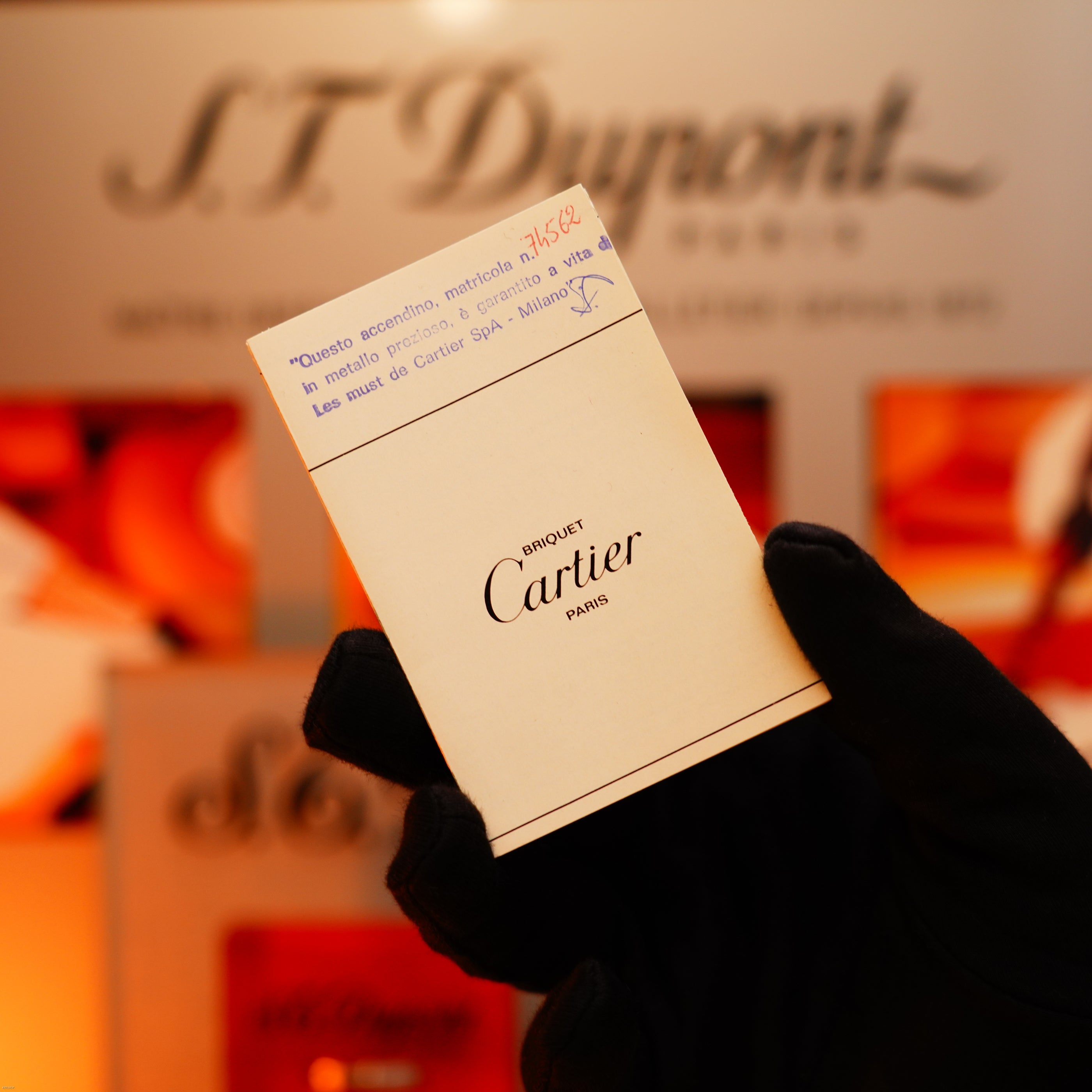 A gloved hand holds a card labeled "Briquet Cartier Paris" with a receipt, set against S.T. Dupont branding—highlighting the Vintage 1970 Early Cartier Production Heavy Silver Finish Rare Guilloché Pattern Lighter by Lucy Lighter.